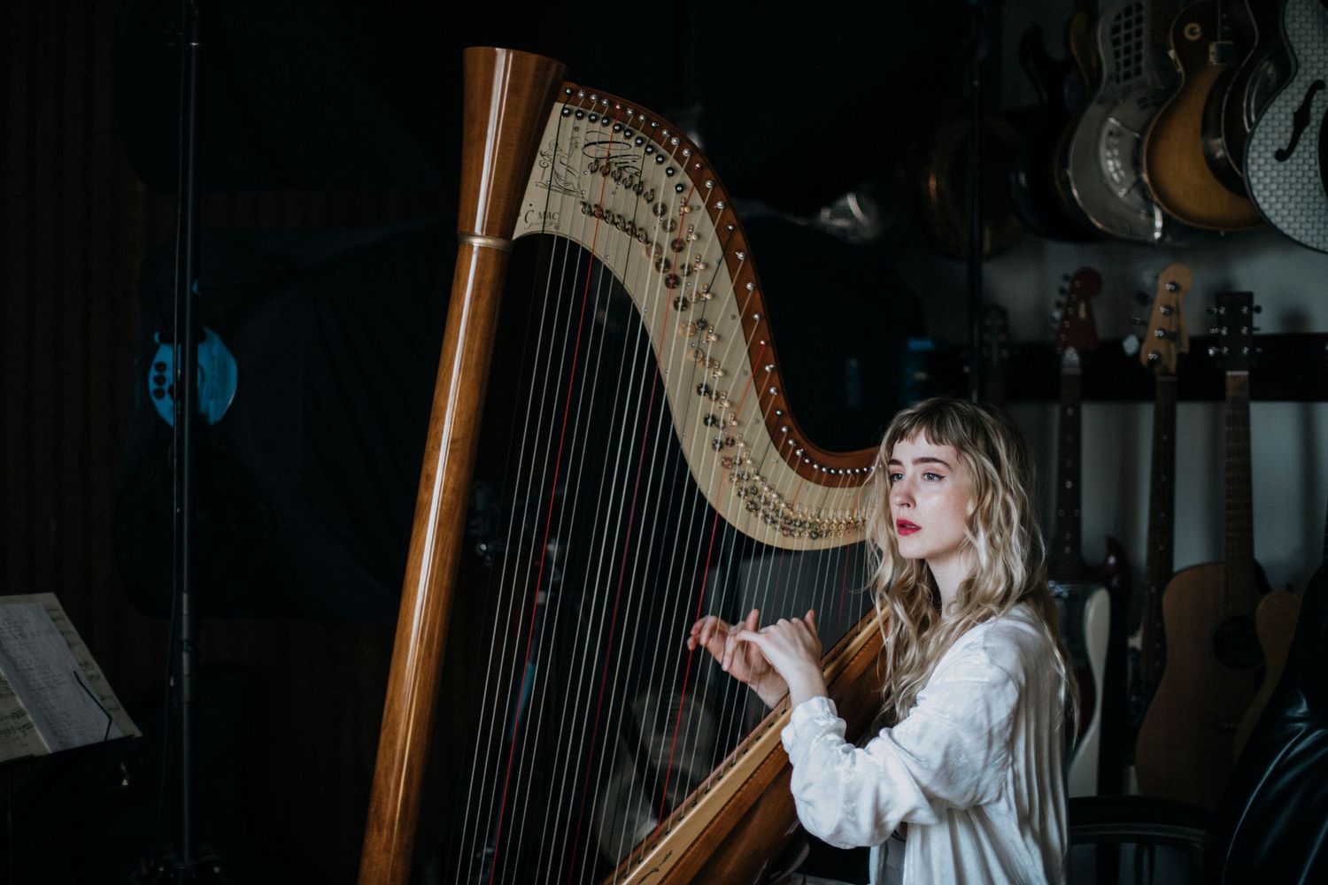 A musician plays a large golden harp in a dimly lit room with dramatic lighting creating an atmospheric scene.