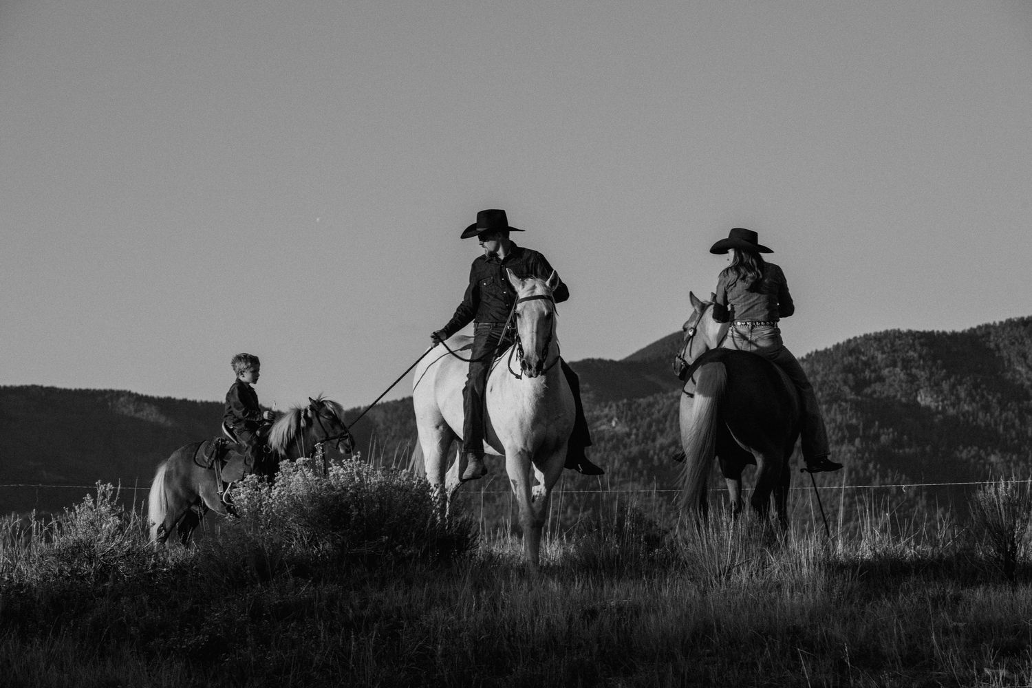 Black and white western lifestyle session in Taos, New Mexico with cowboys on horseback against a mountain landscape