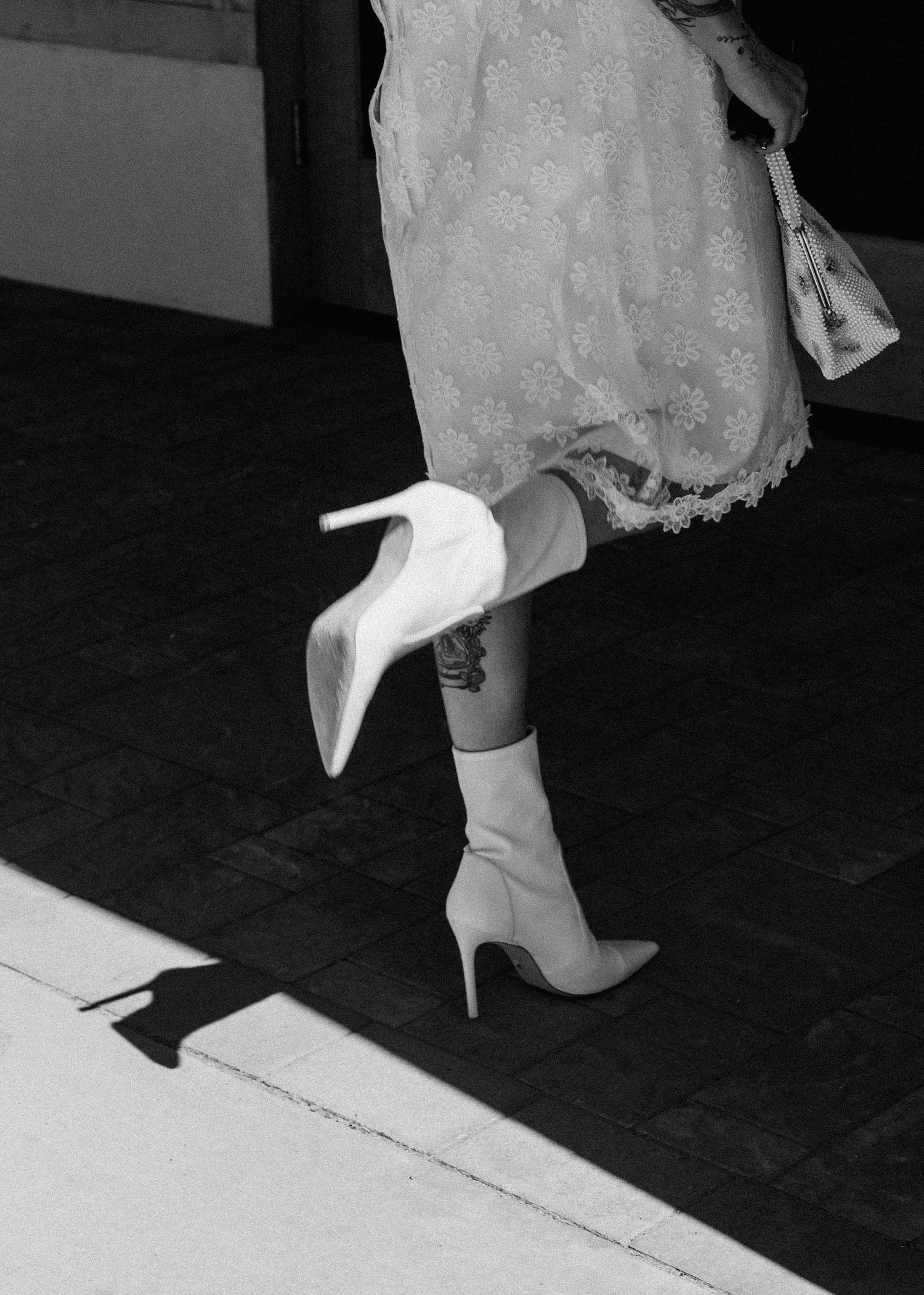 Black and white photo showing a series of white high heels stepping on a dark surface.
