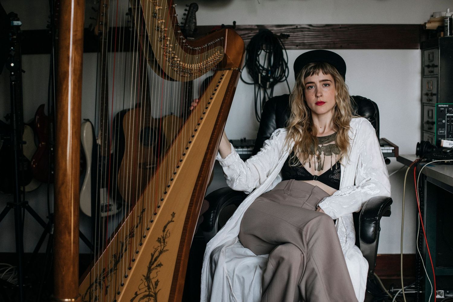 A musician plays a classical harp in a dimly lit room while wearing a white flowing dress.