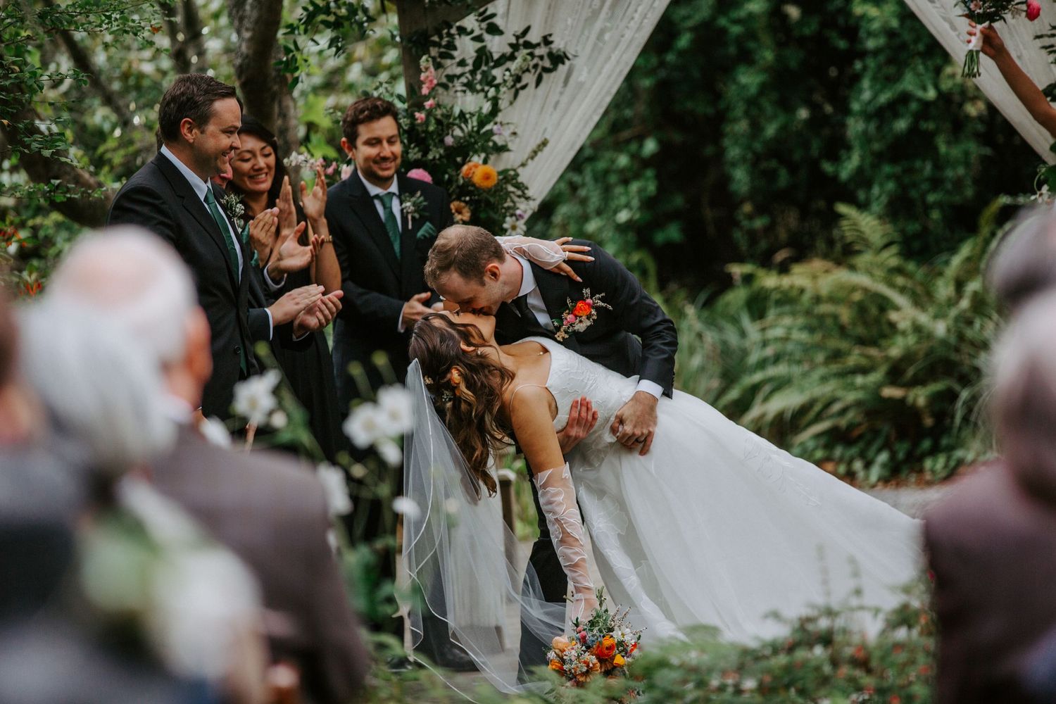 Joyful outdoor wedding ceremony under white fabric draped between trees.
