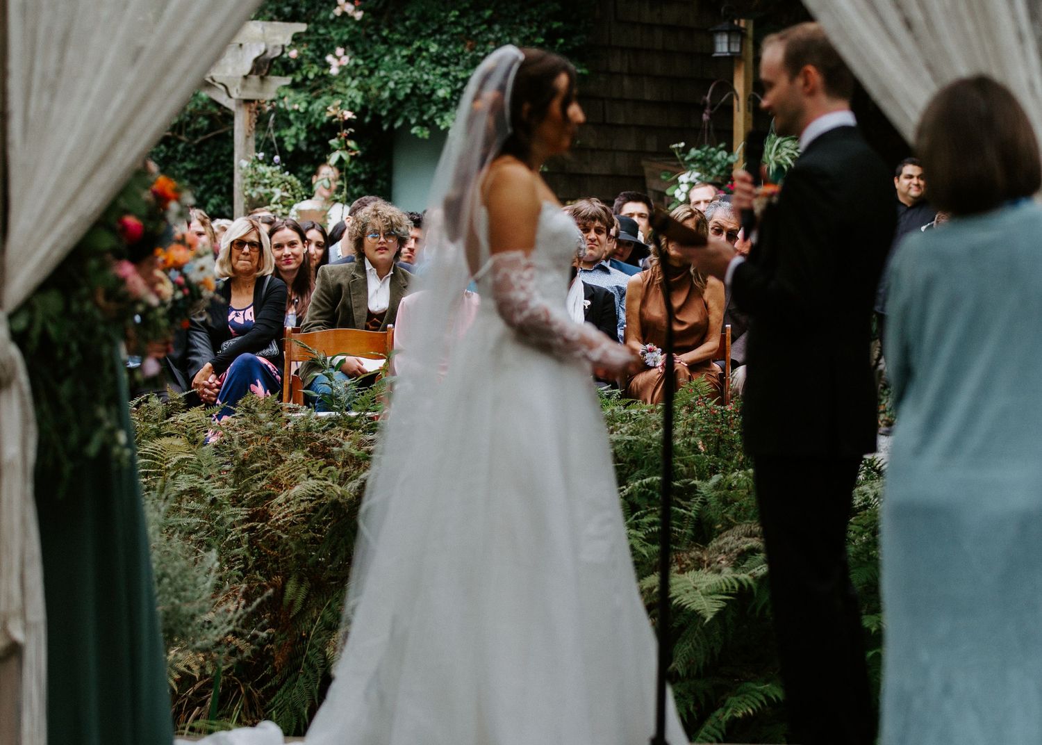 Wedding ceremony scene in a garden setting with bridesmaids in light blue dresses and white floral arrangements.