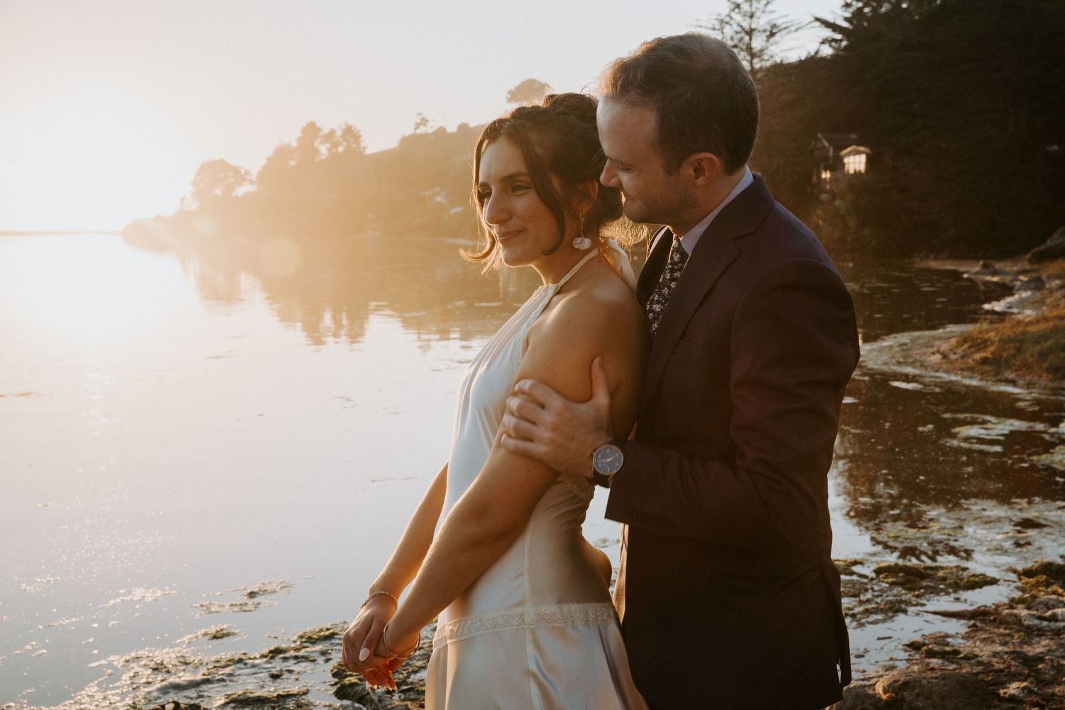 Romantic sunset silhouettes of a couple embracing on a rocky beach during their wedding photoshoot.