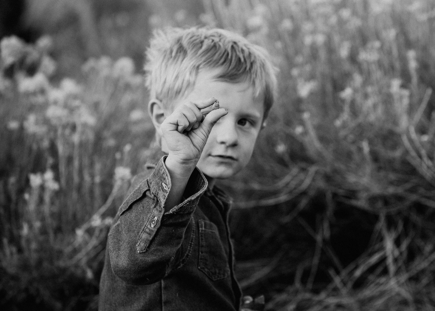 Black and white portrait of a child in nature touching their face with a thoughtful expression.