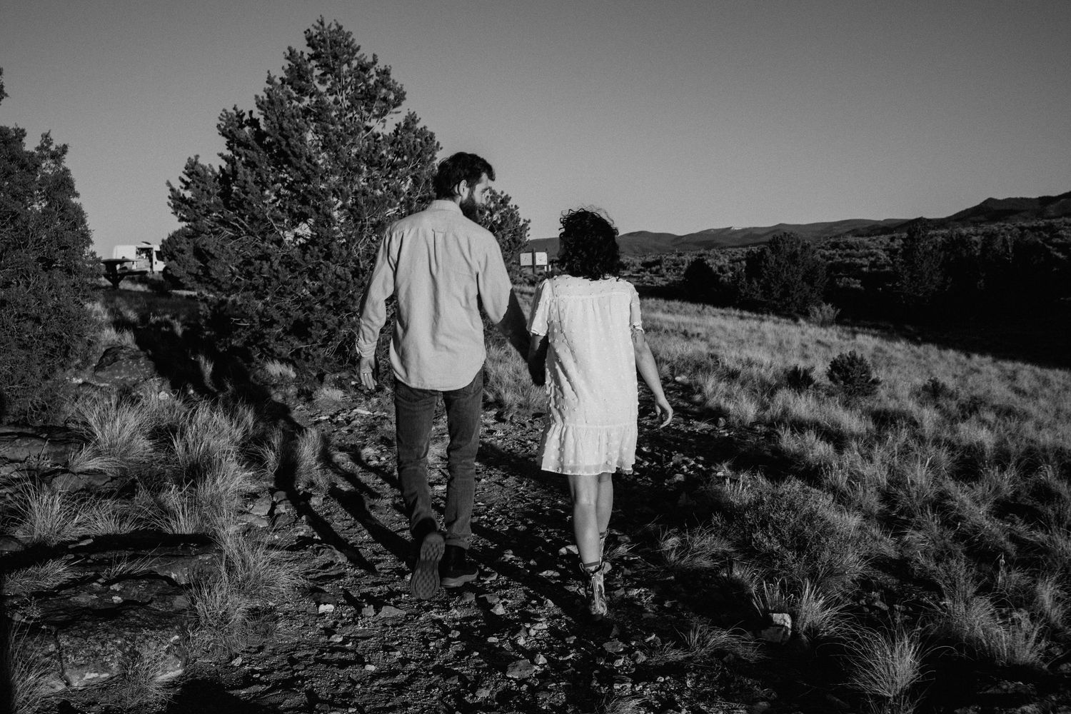 Black and white engagement session in Taos, New Mexico with couple walking hand in hand along a mountain trail