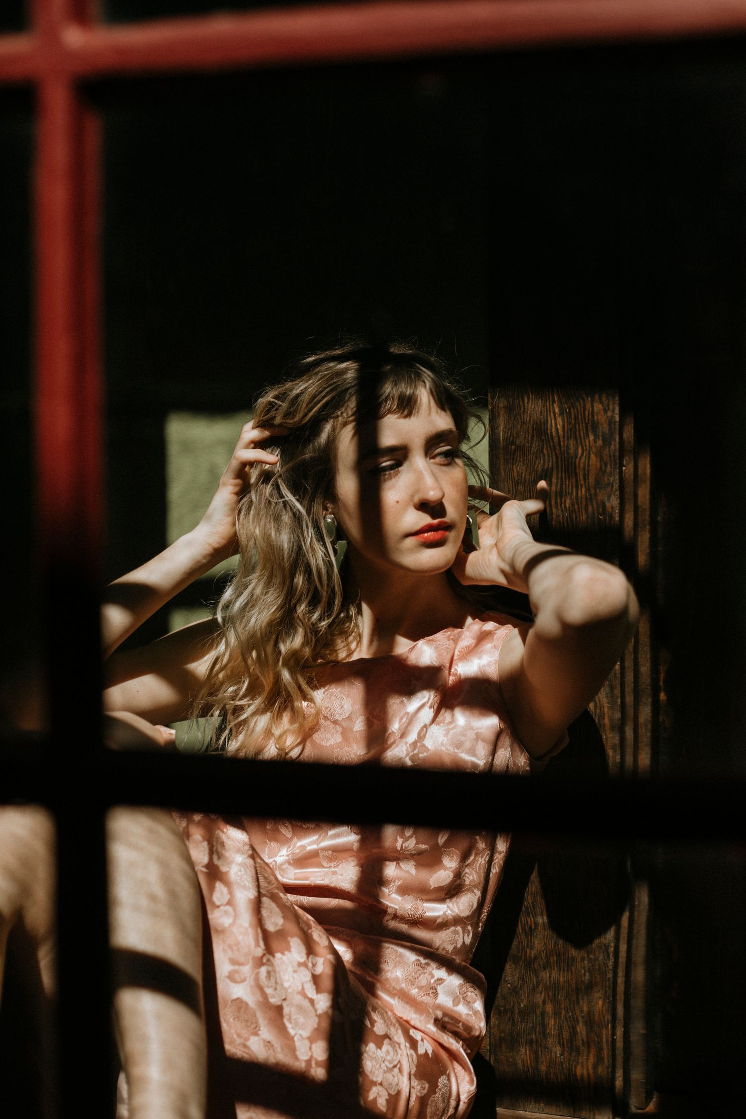 Artistic portrait of someone in a vintage dress with dramatic shadows and window bars creating a moody atmosphere.