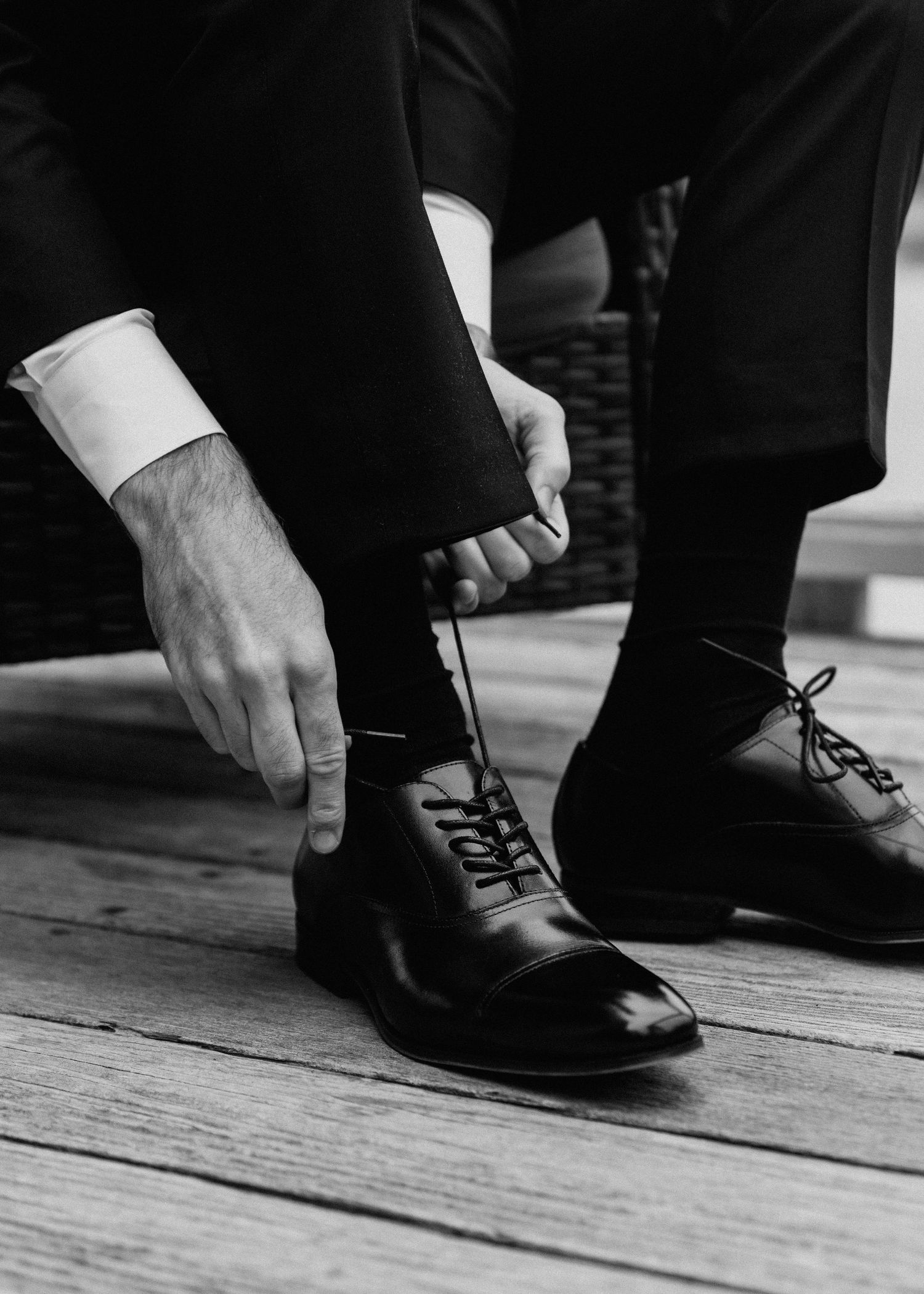 Close-up sequence of formal black dress shoes being tied on wooden floor.