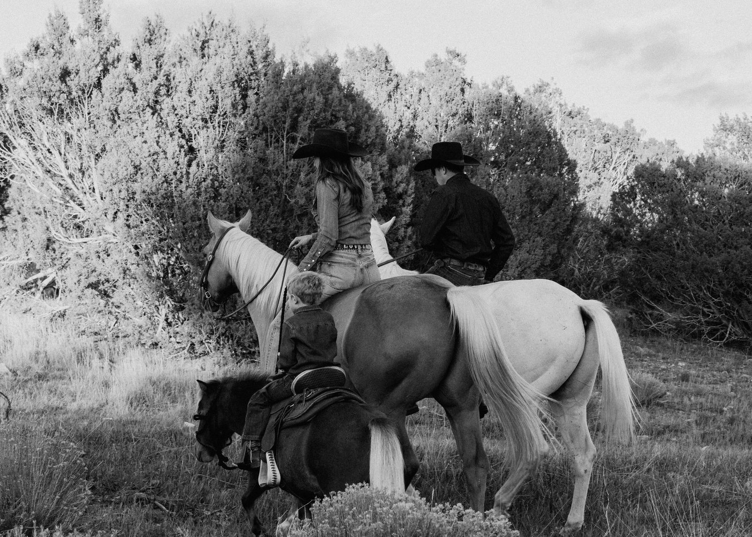 Black and white western lifestyle session in Taos NM with riders on horseback along a scenic trail
