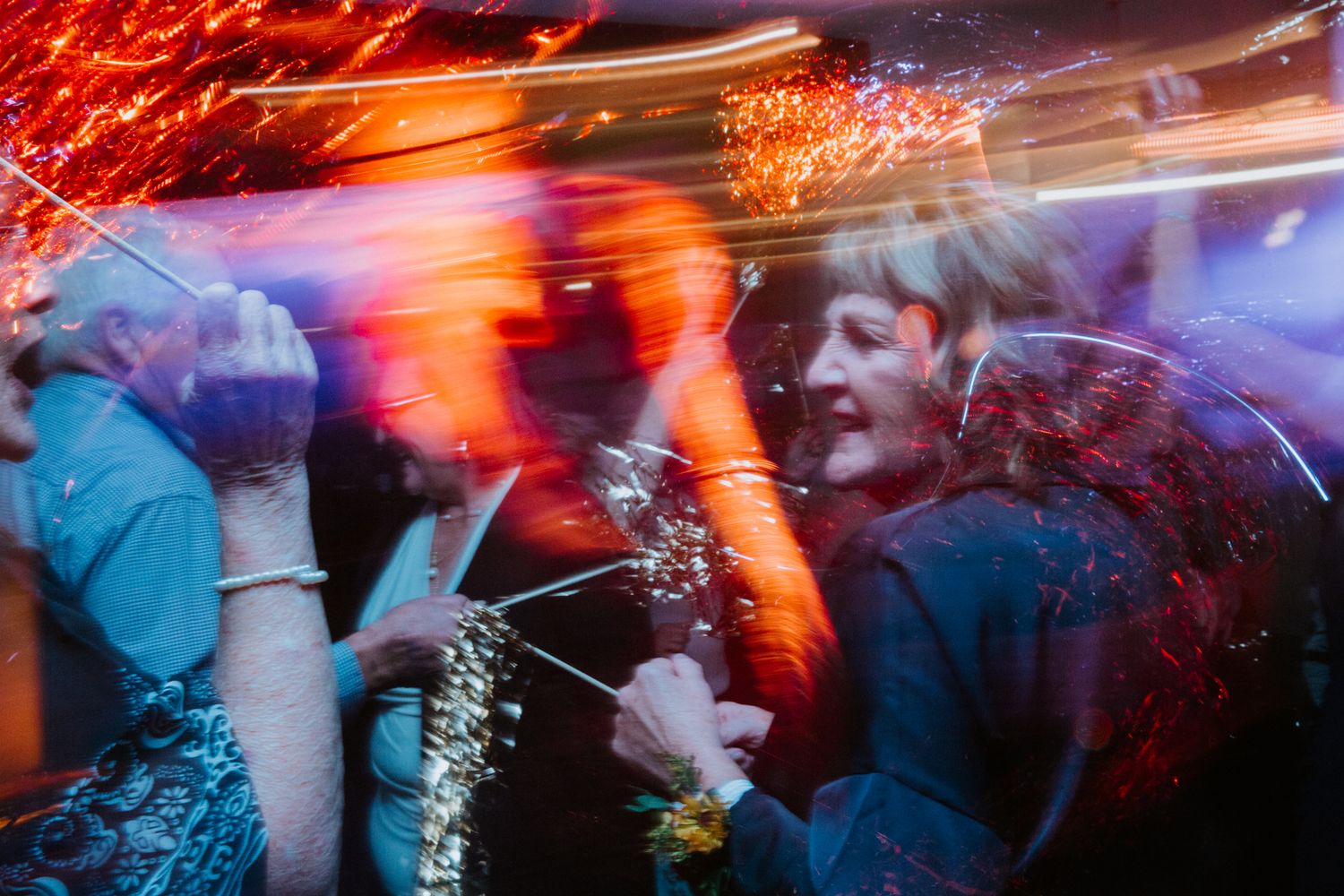 Long exposure photograph shows colorful light trails and motion blur at a nighttime event with dancing silhouettes.
