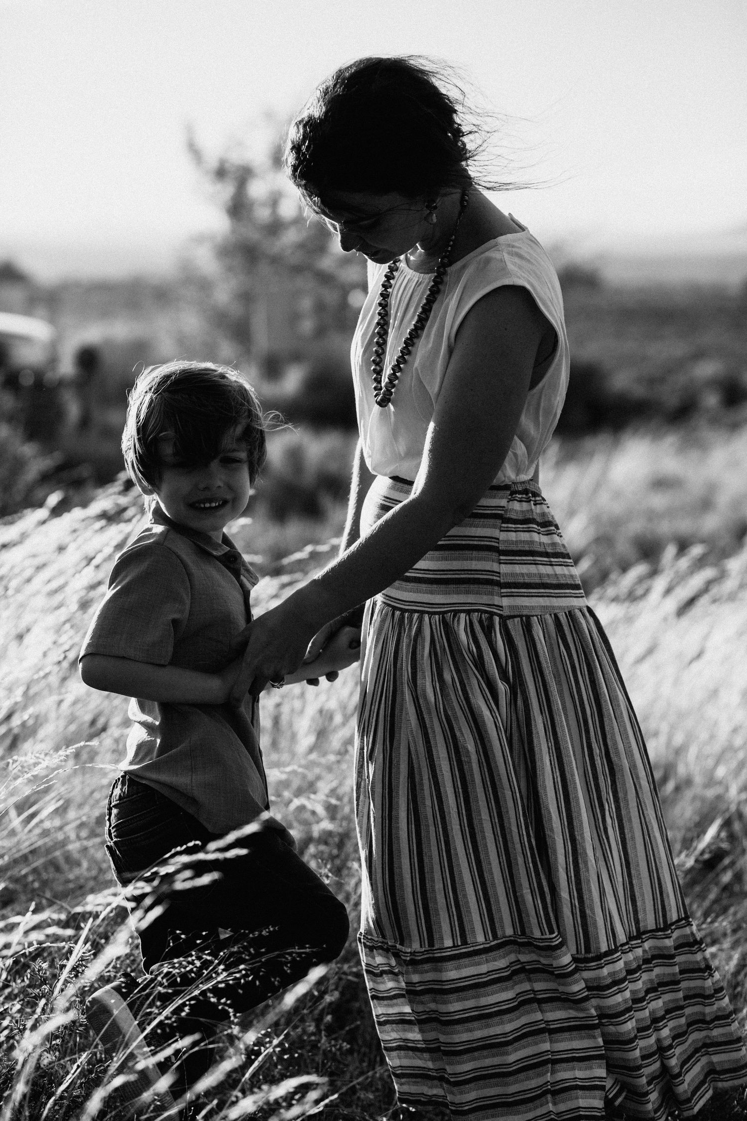 Black and white photo series showing tender moments between parent and child in a sunlit field of tall grass.