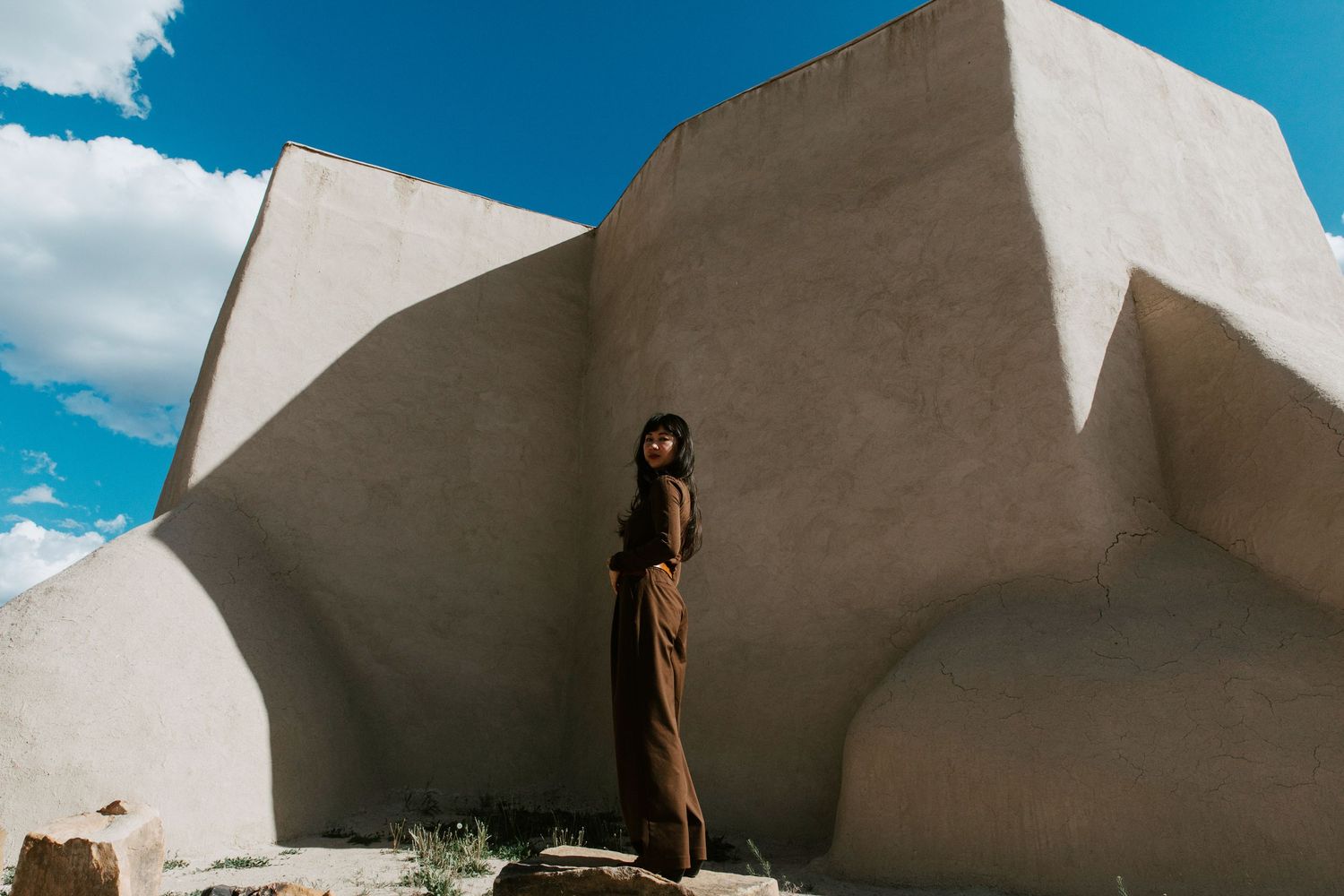 Woman in brown outfit standing against white adobe building walls under blue sky.
