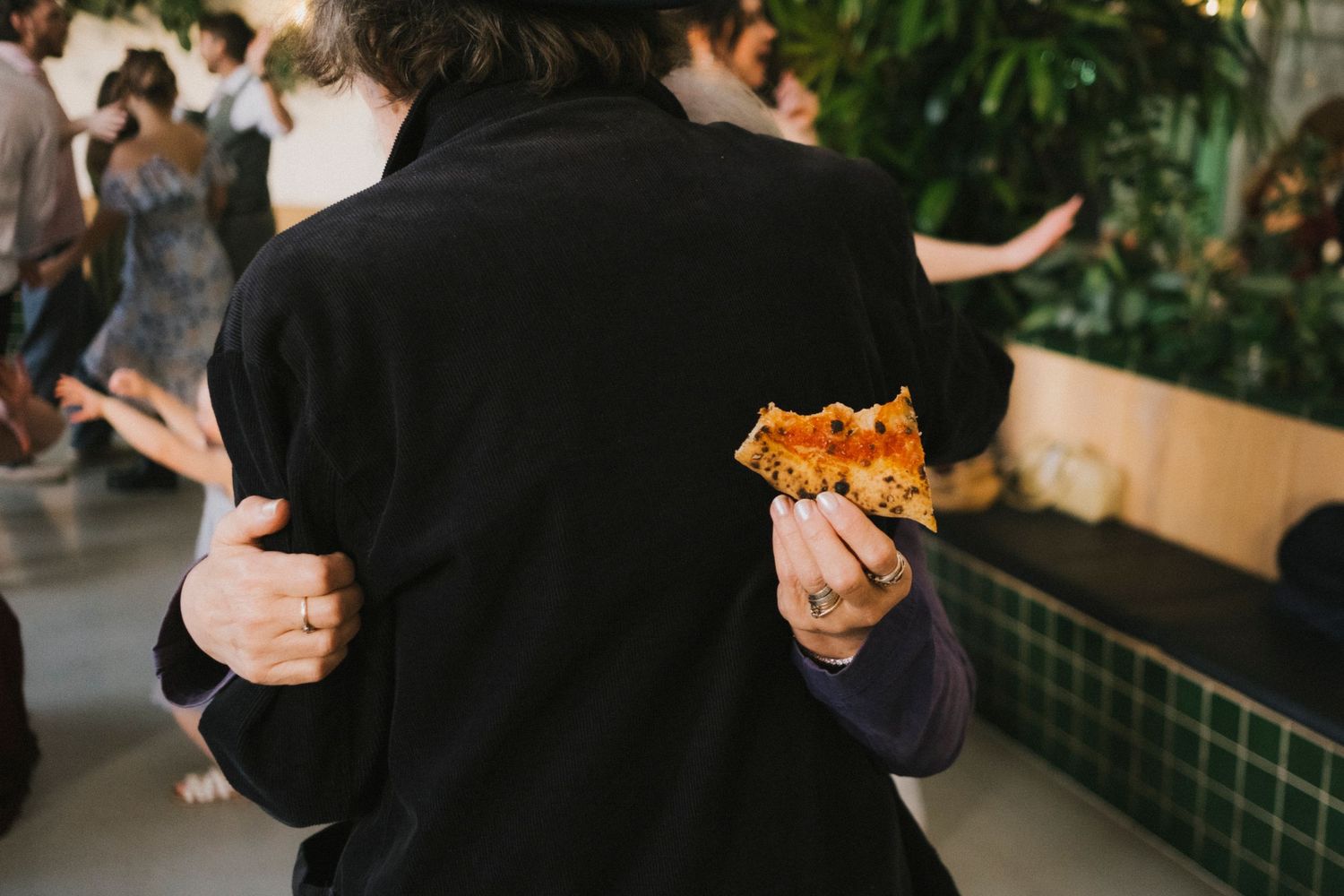 Guest holding a slice of pizza while slow dancing with a partner at a lively wedding reception.