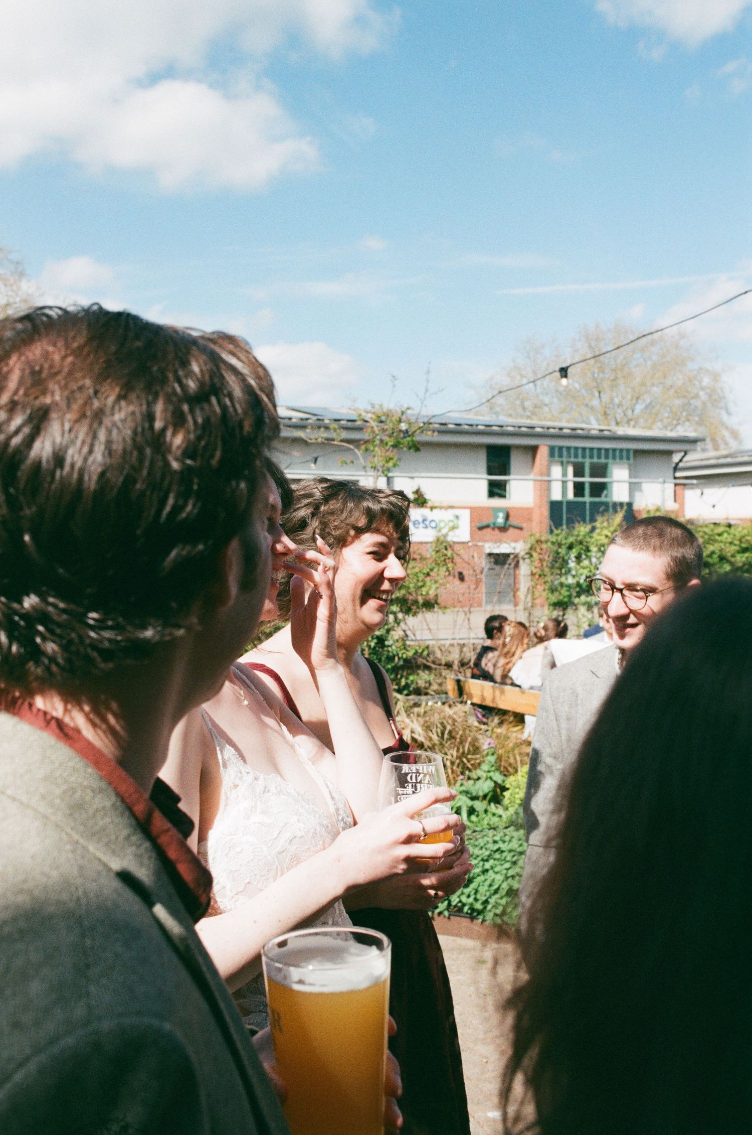 Group of friends laughing and drinking beer outdoors at a sunny garden party.