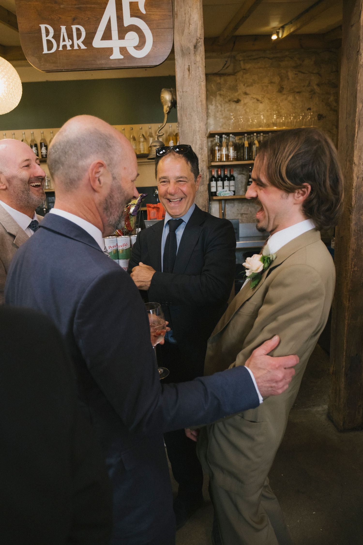 Men in suits socializing and laughing together near Bar 45 at a wedding reception.