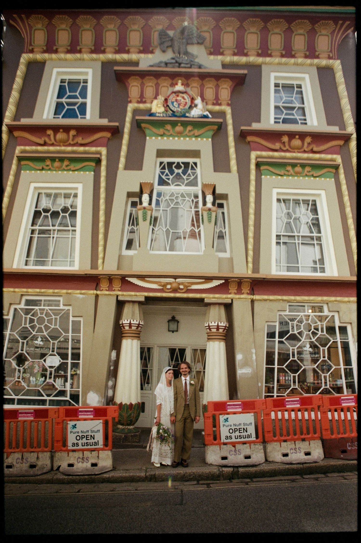 Bride and groom posing outside an ornate colorful building with construction barriers during their wedding day.