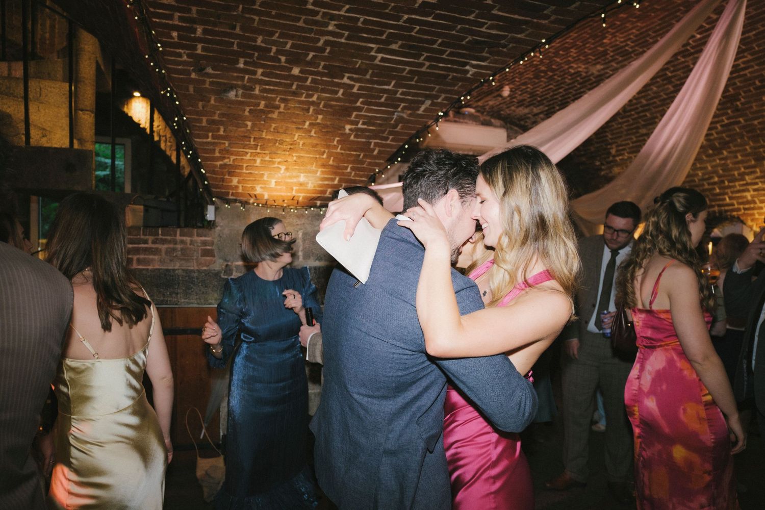 Couple sharing a romantic kiss on the dance floor during a warmly lit wedding reception.