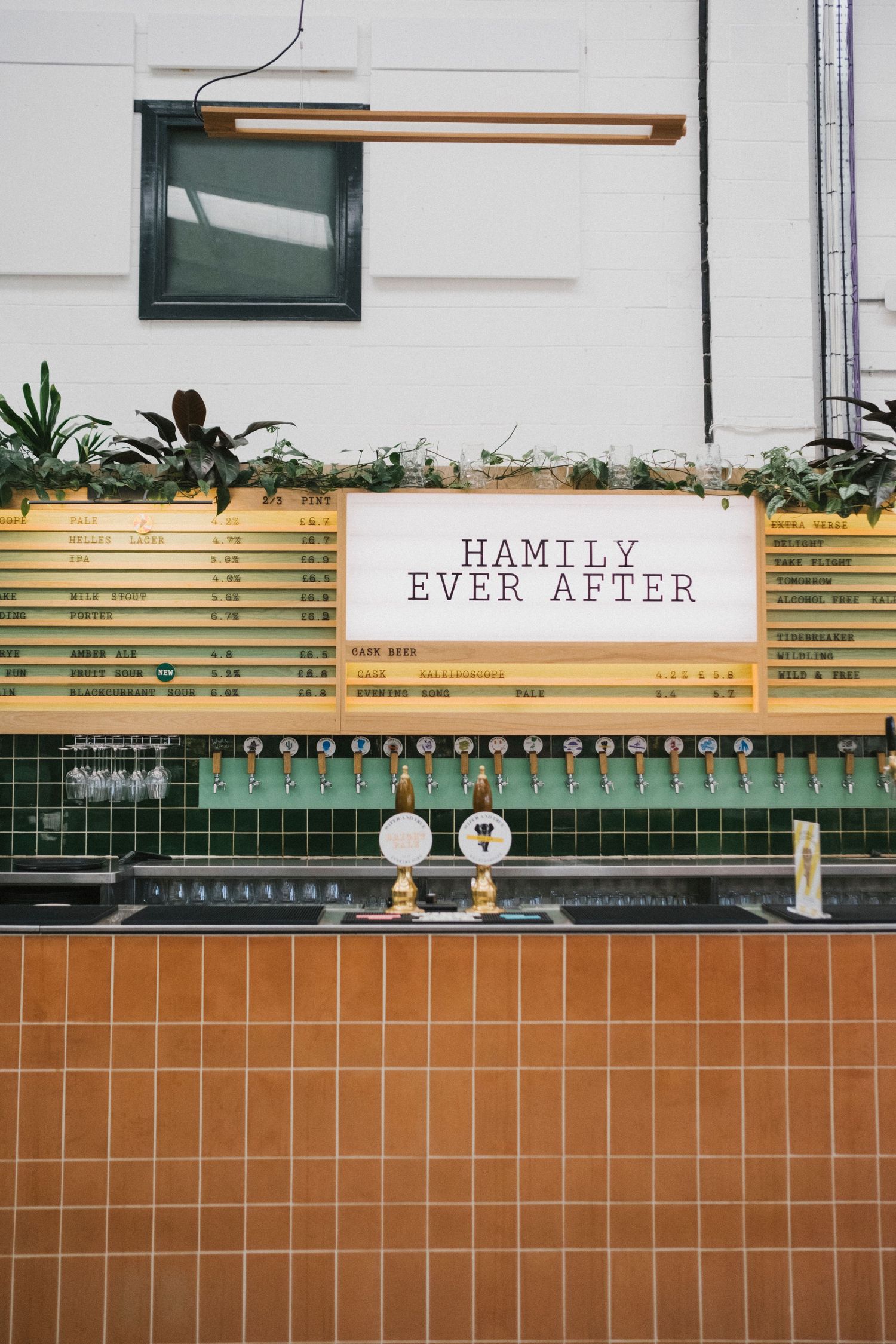 A bar counter with green tiles and beer taps displaying a 