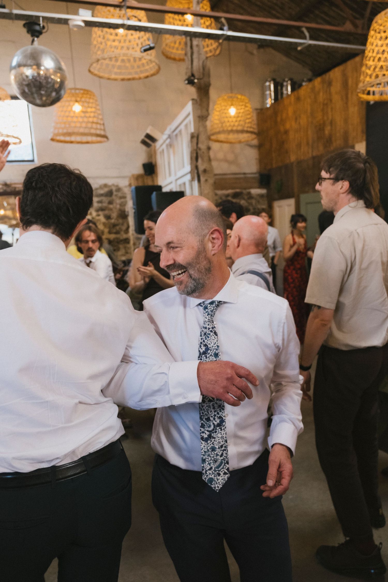 Guests dancing and celebrating at a wedding reception in a rustic venue with disco ball lighting.