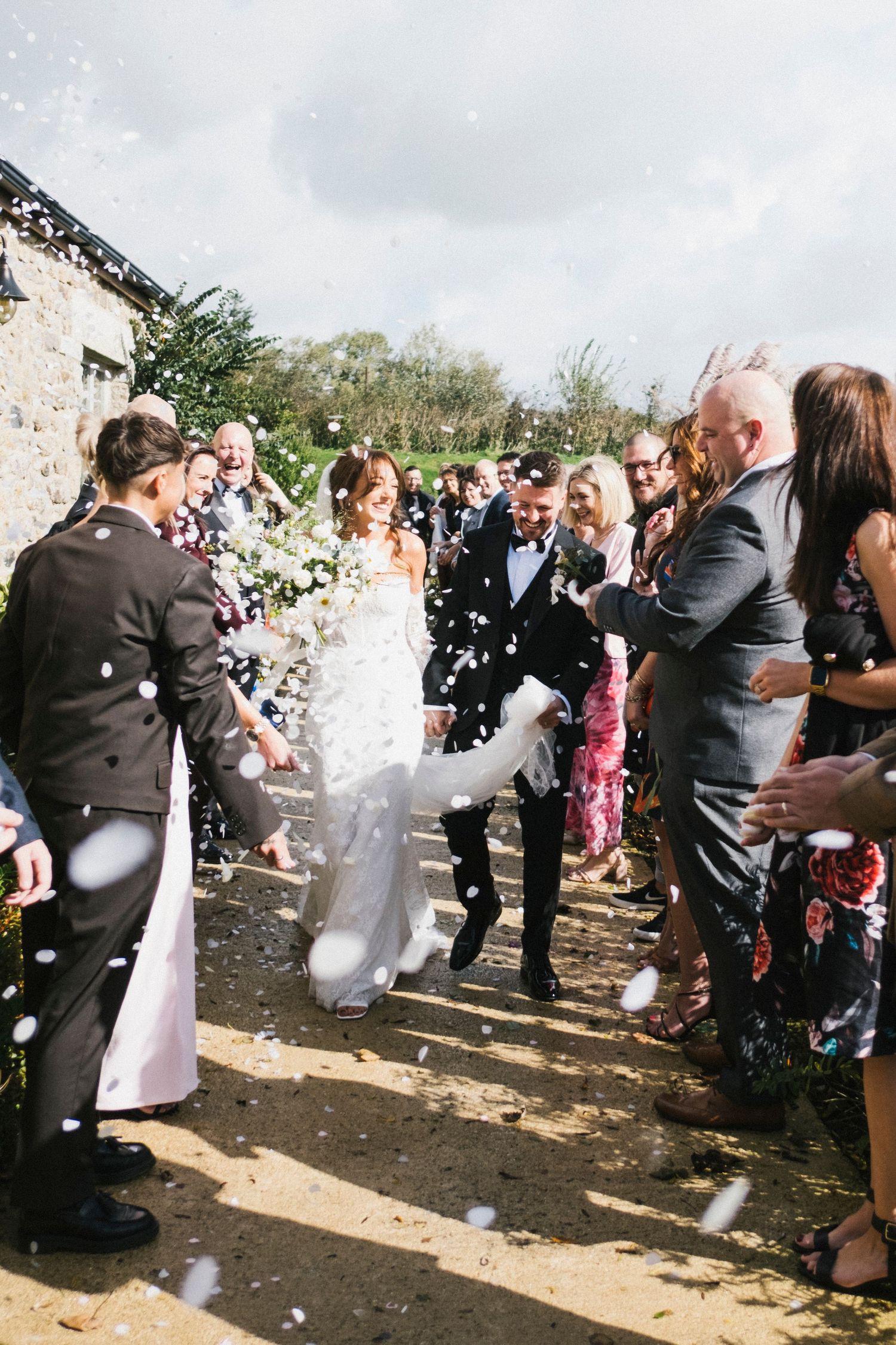 Bride and groom walk through a joyful confetti shower surrounded by cheering wedding guests.