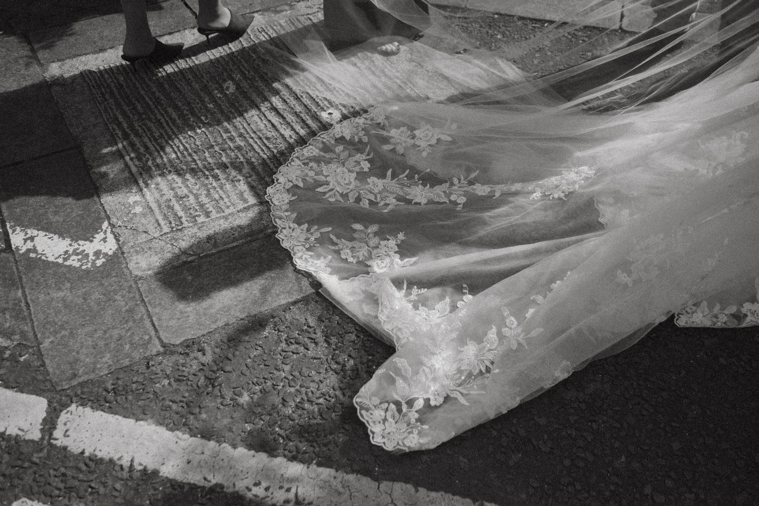 Black and white photo of a flowing wedding dress train spread across a crosswalk pavement.
