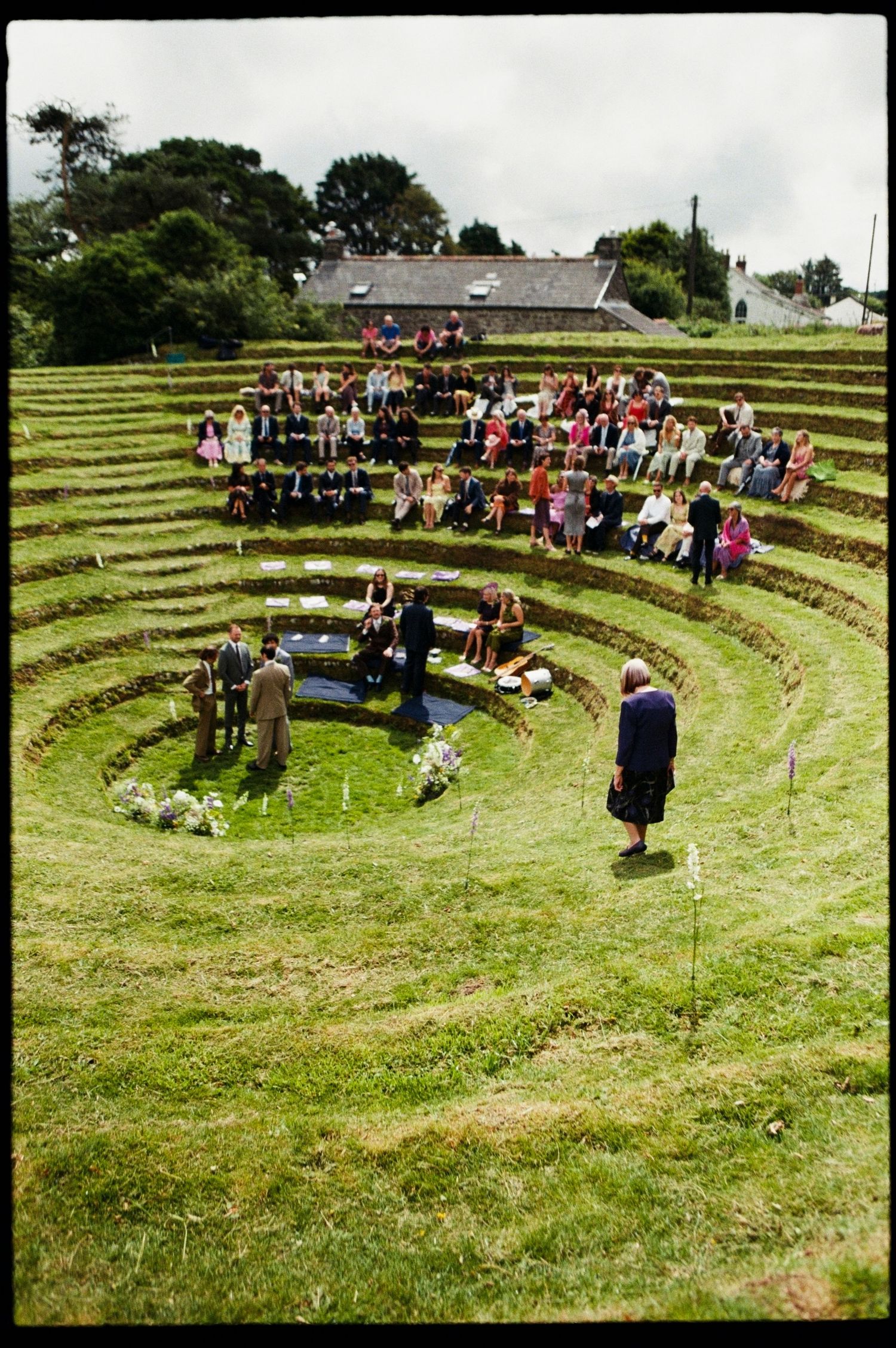 Outdoor wedding ceremony in a terraced grass amphitheater with guests seated on tiered levels.