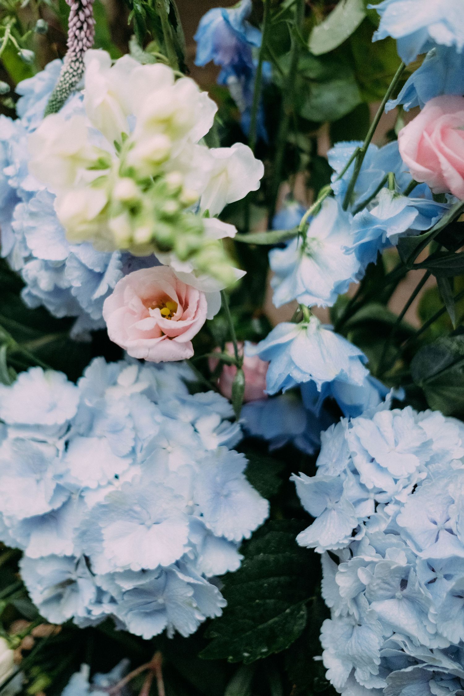 Elegant wedding floral arrangement featuring soft blue hydrangeas, pink roses, and white blooms with lush green foliage.