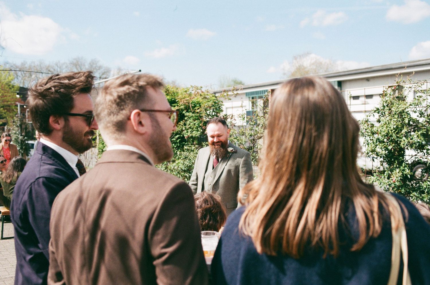 Group of elegantly dressed guests socializing outdoors at a sunny garden wedding reception.