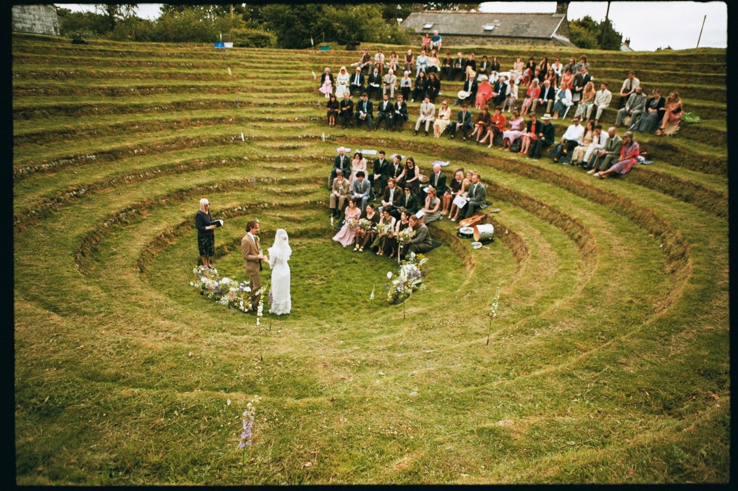 Aerial view of an outdoor amphitheater with terraced grass seating hosting a ceremony with guests gathered in a circle.