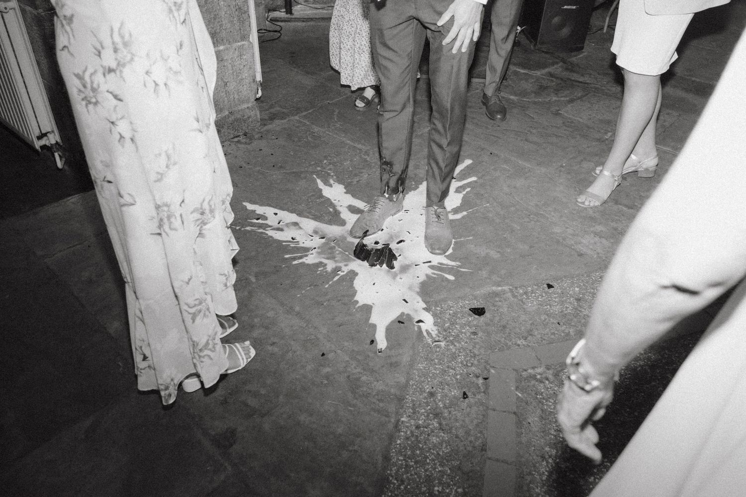 Black and white photo of a wedding cake dropped and smashed on the floor at a reception.