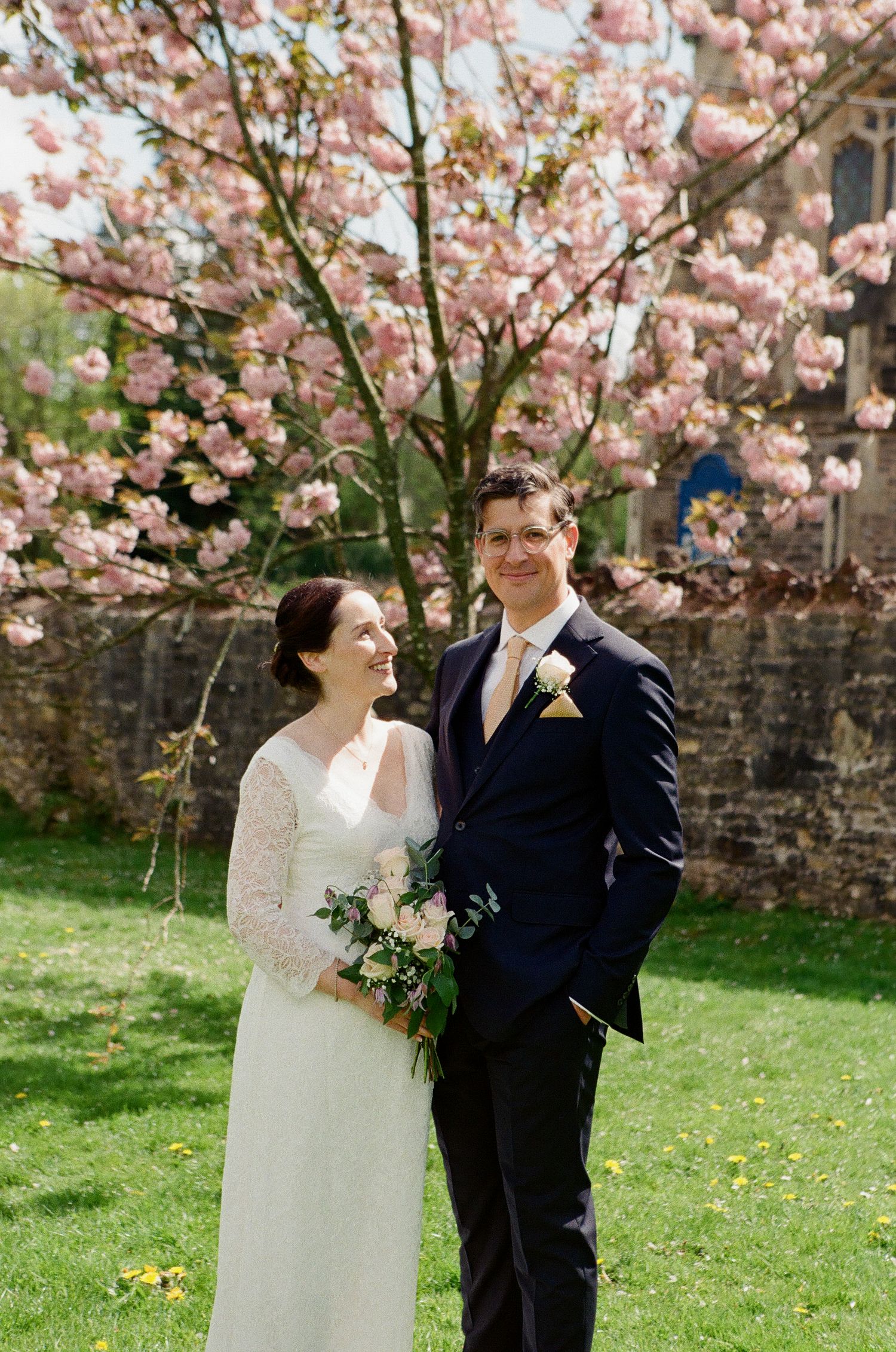Bride and groom smiling together beneath a stunning pink cherry blossom tree on their wedding day.