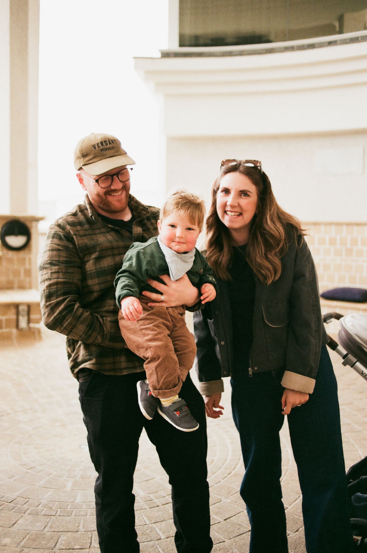 A smiling family with a young child poses together outdoors in casual winter clothing.