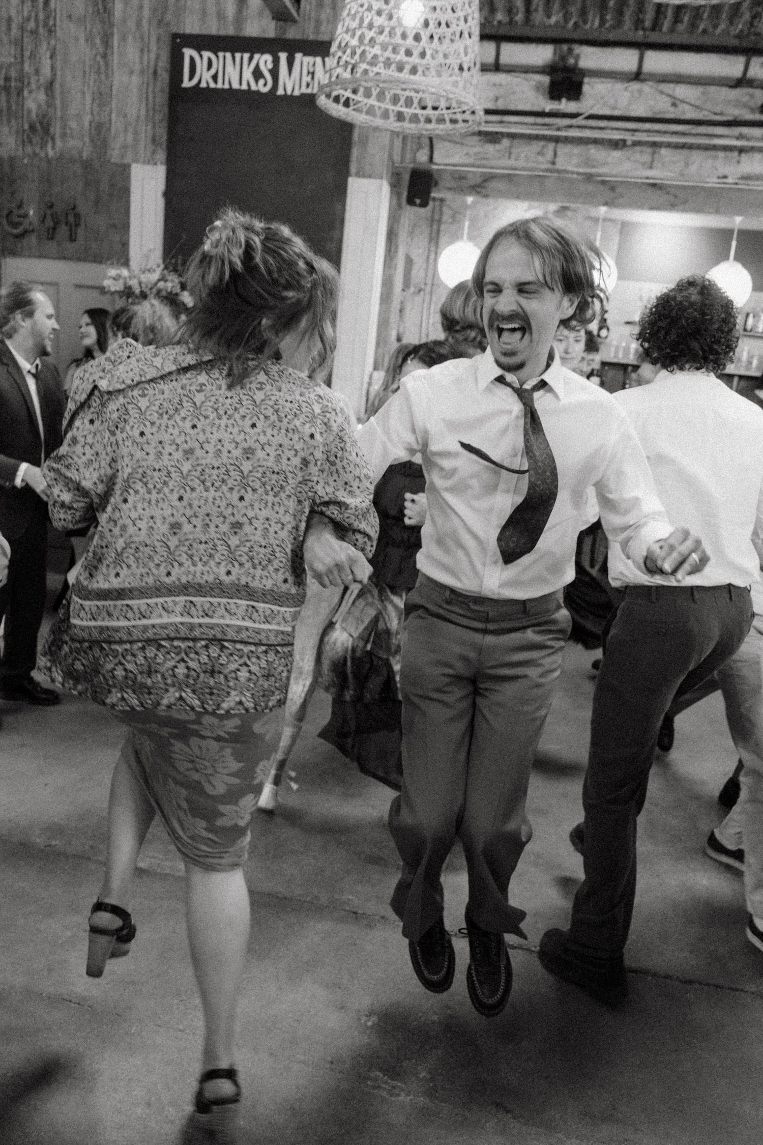 Man dancing energetically with tie flying at a lively black and white wedding reception.