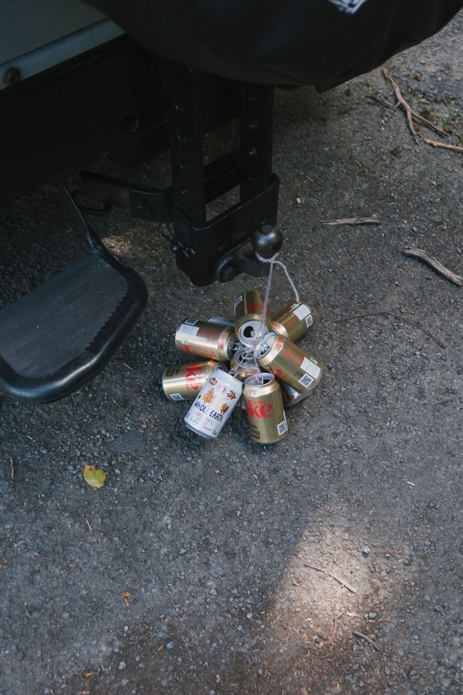 Empty beer cans tied together hang from a vehicle trailer hitch as a wedding car decoration.
