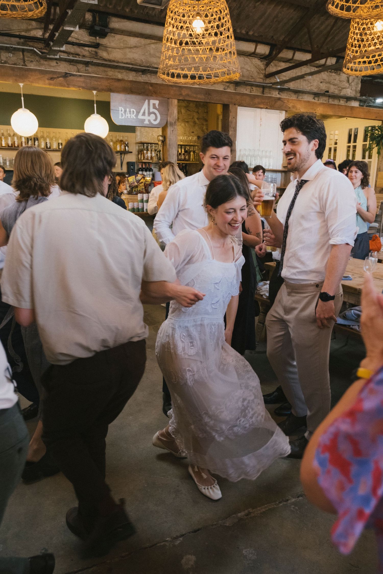 Bride dancing joyfully with guests at a lively indoor wedding reception.