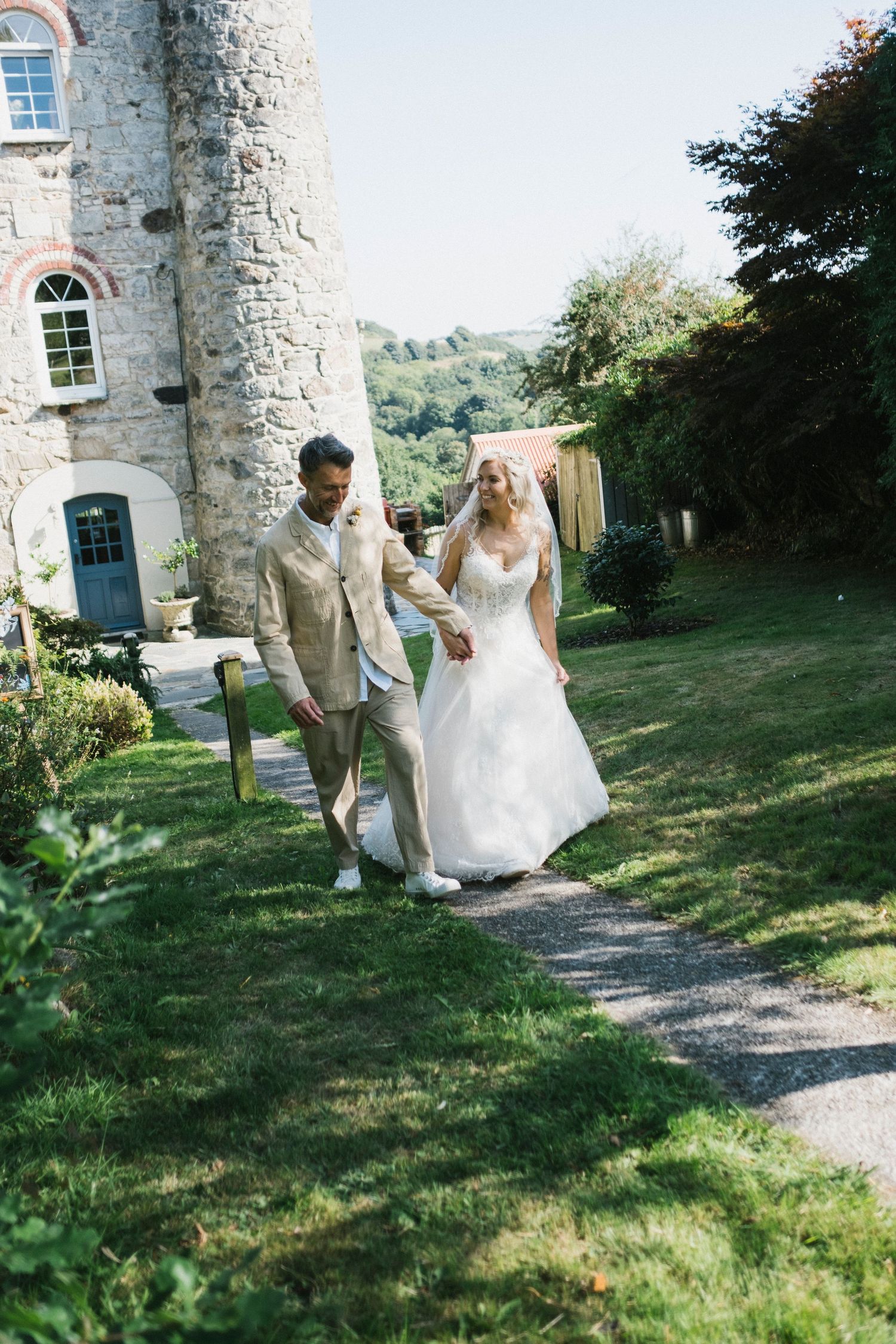 Bride and groom walking hand in hand through castle gardens on their wedding day in elegant outdoor setting.