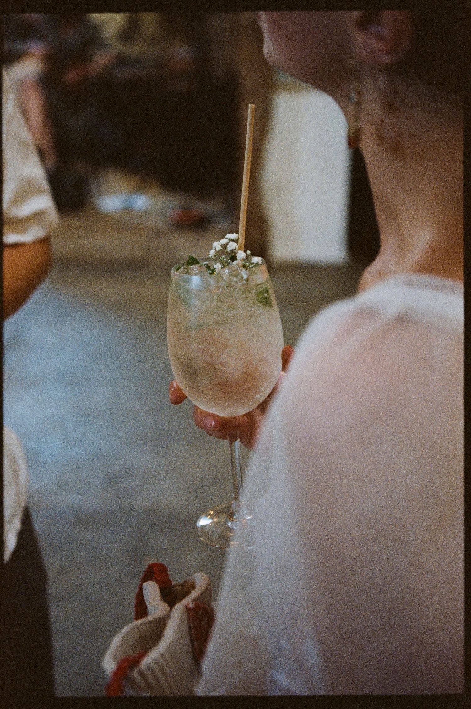 A woman holds an elegant cocktail garnished with flowers and a bamboo straw at a social event.