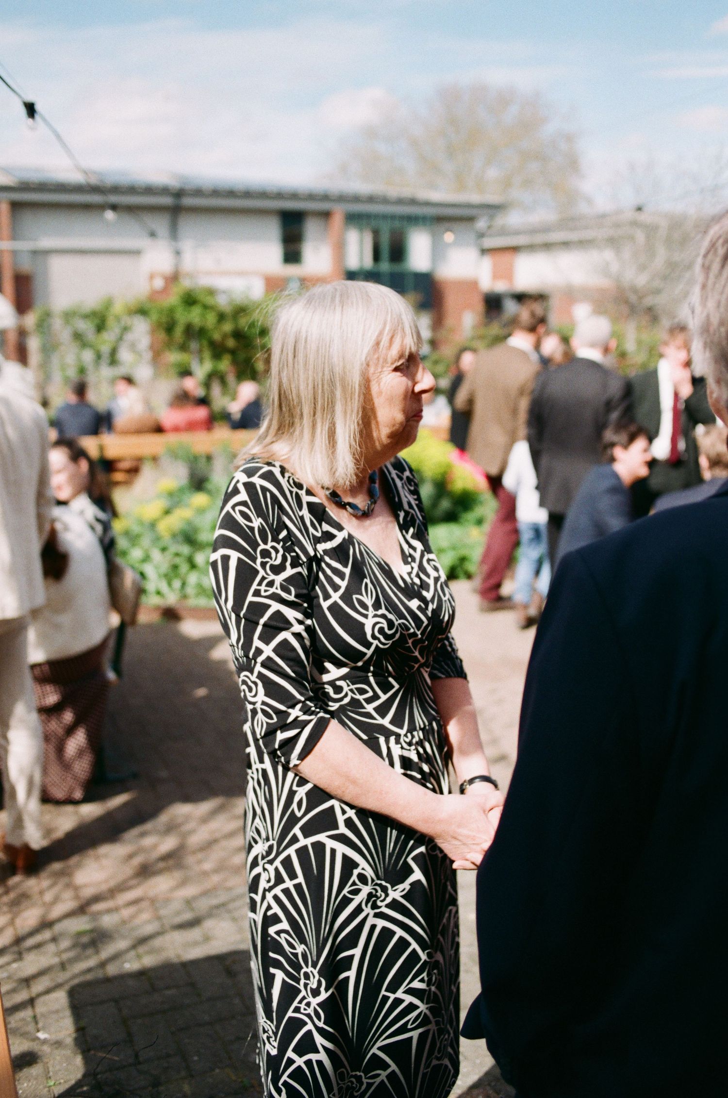 Woman in black and white patterned dress at an outdoor garden party event on a sunny day.