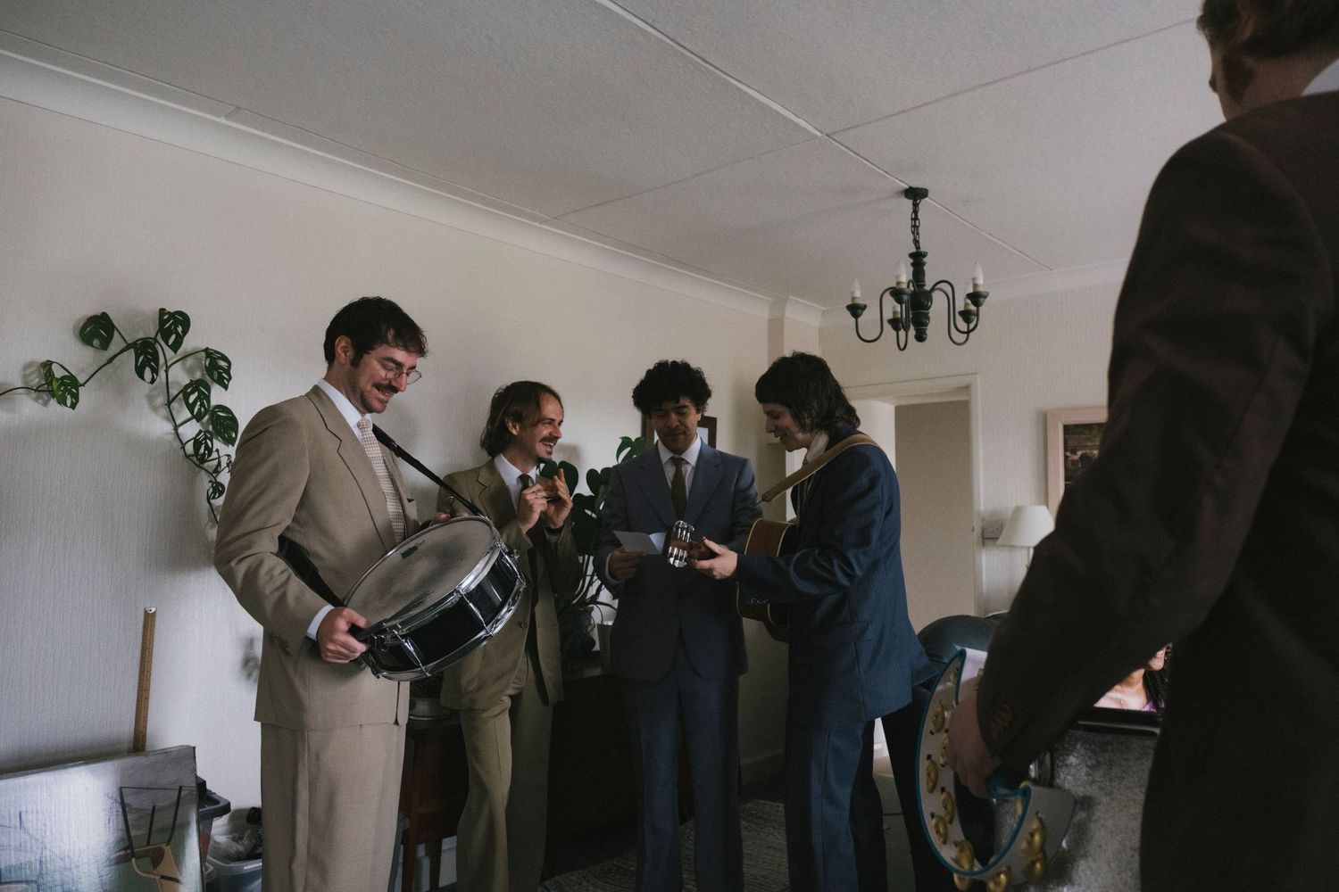 Groomsmen gathered indoors playing musical instruments during wedding day preparations.