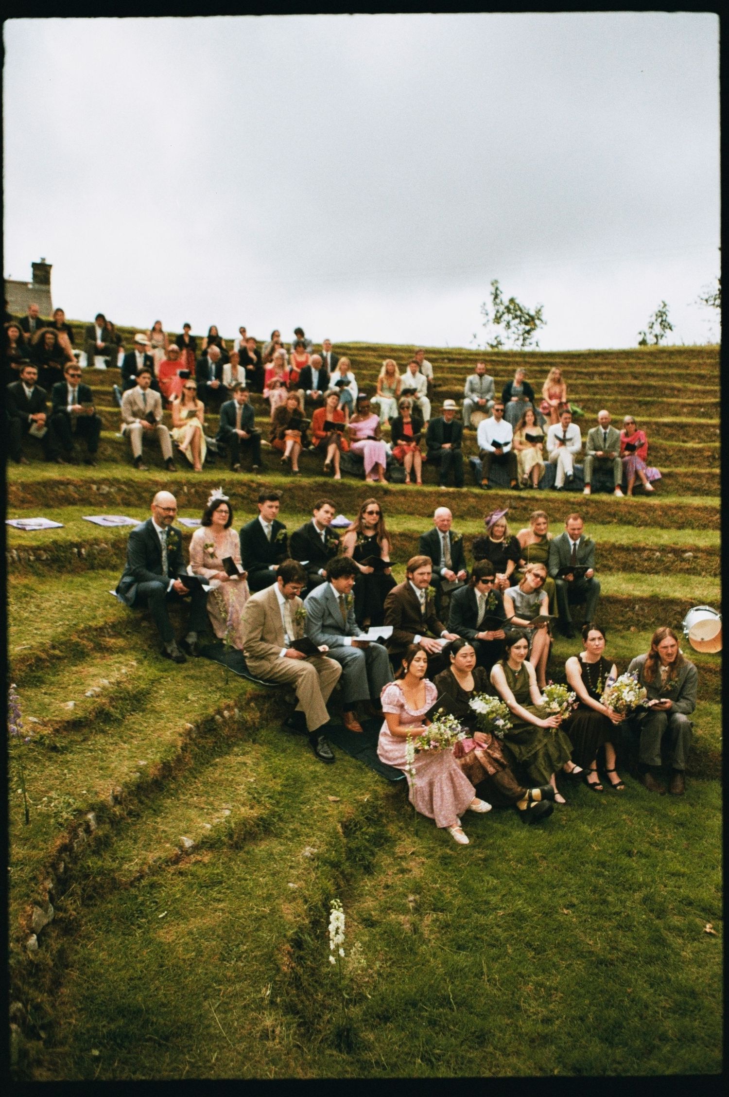 Wedding guests seated on grass terraces watching an outdoor ceremony in a natural amphitheater.