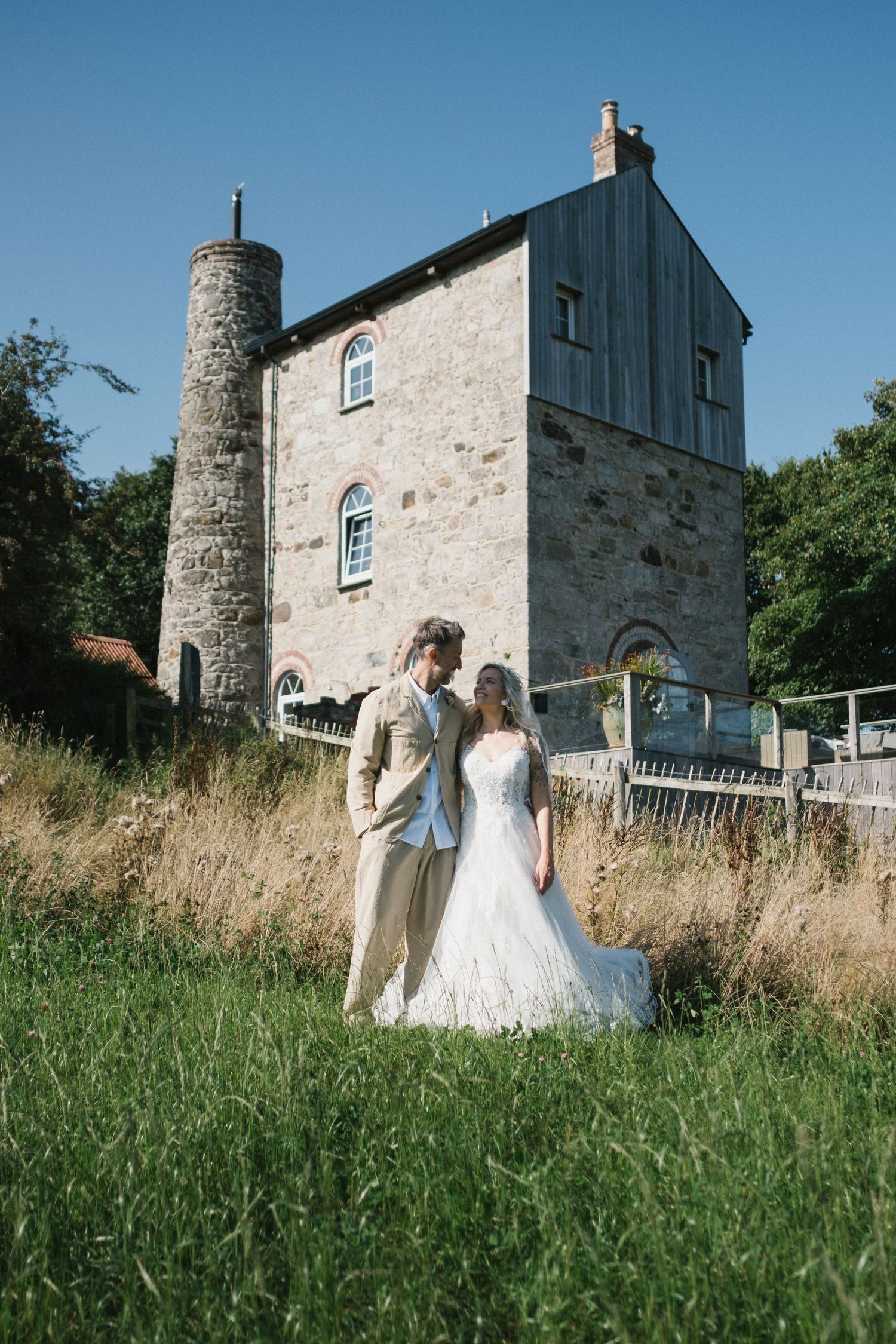 Bride and groom pose together in front of a historic stone building on their wedding day.