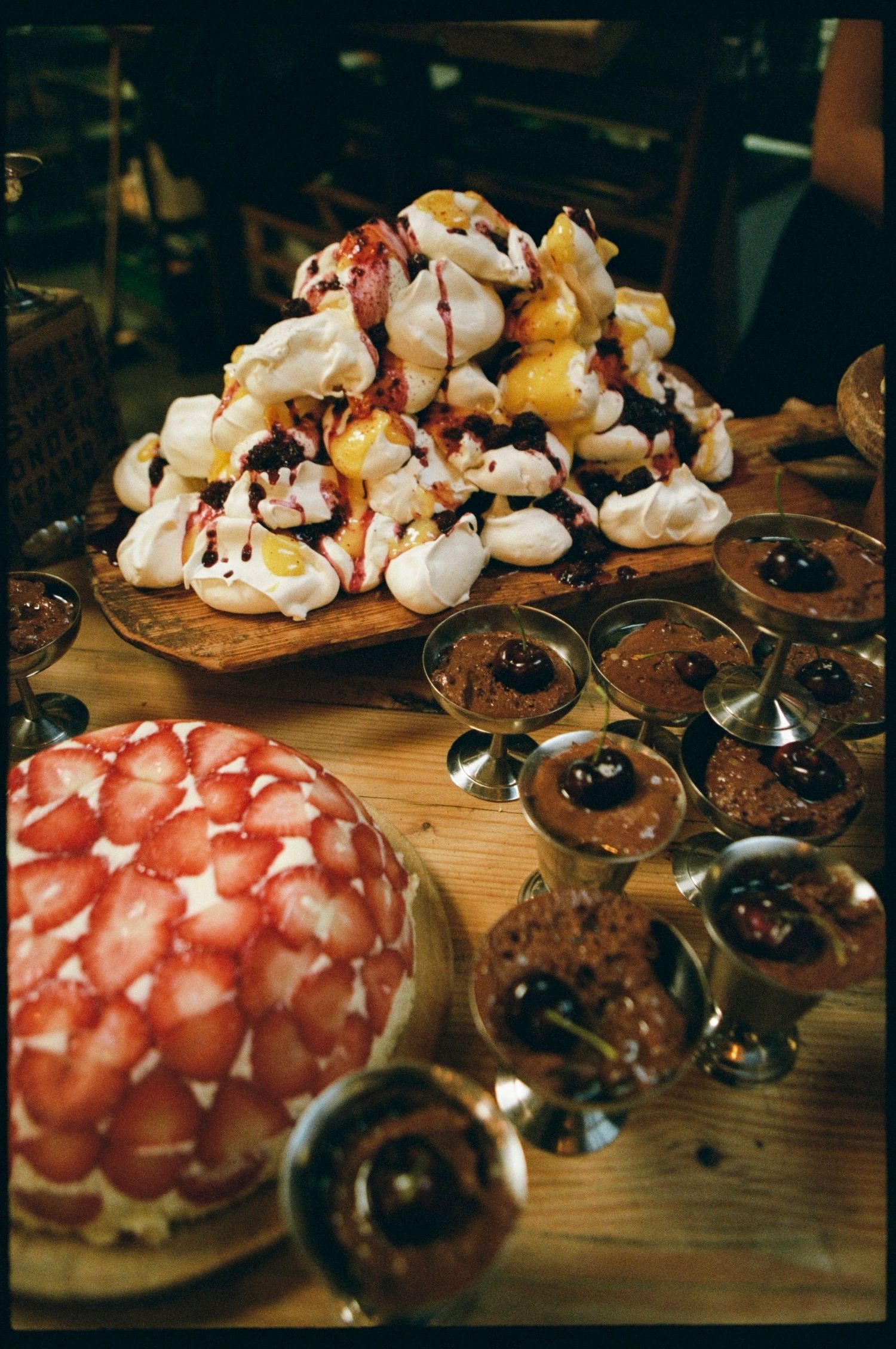 Elegant wedding dessert table featuring a strawberry cake, pavlova tower, and chocolate mousse cups.