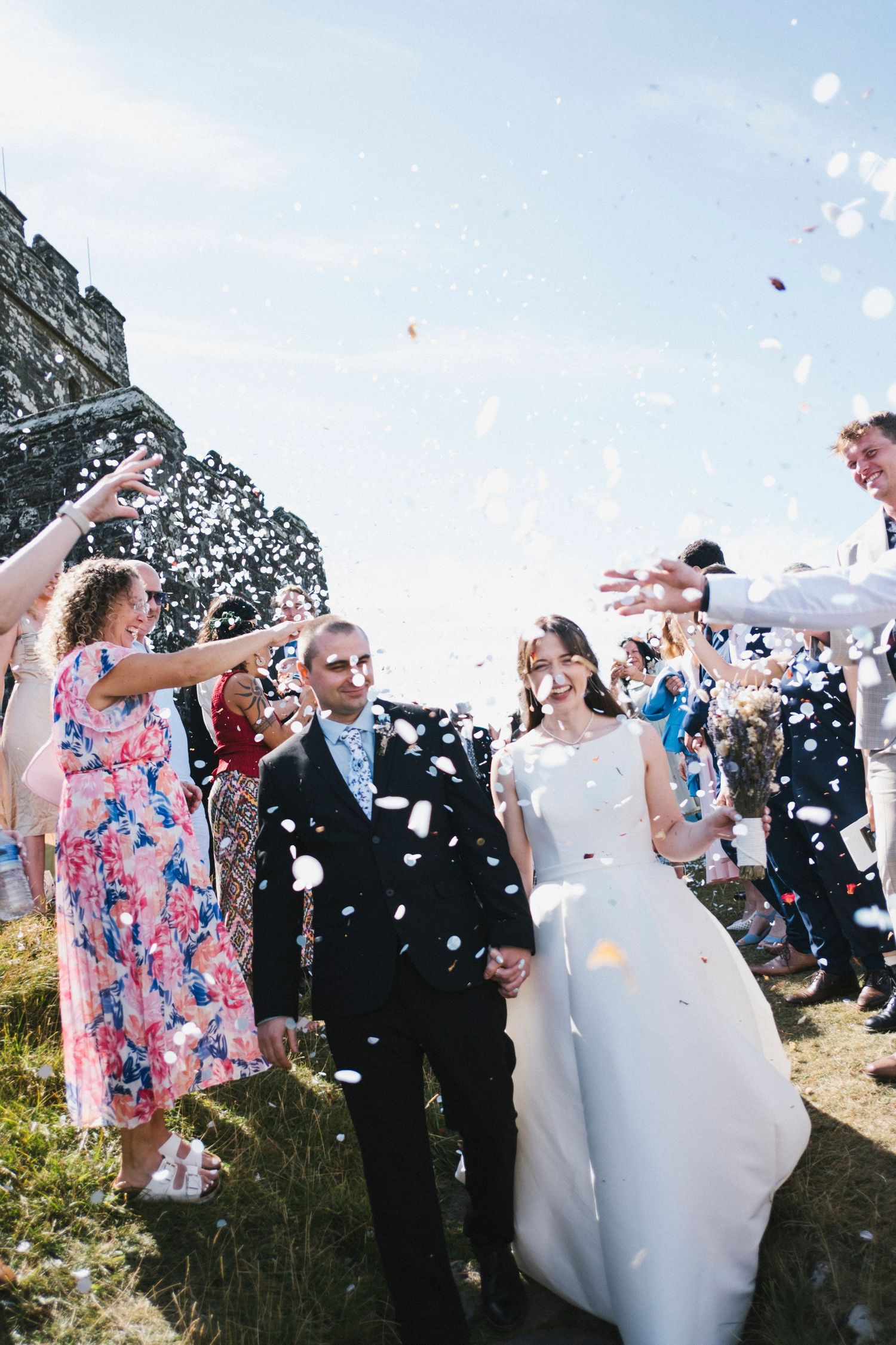 Joyful newlyweds walk through a shower of white confetti thrown by cheering wedding guests.