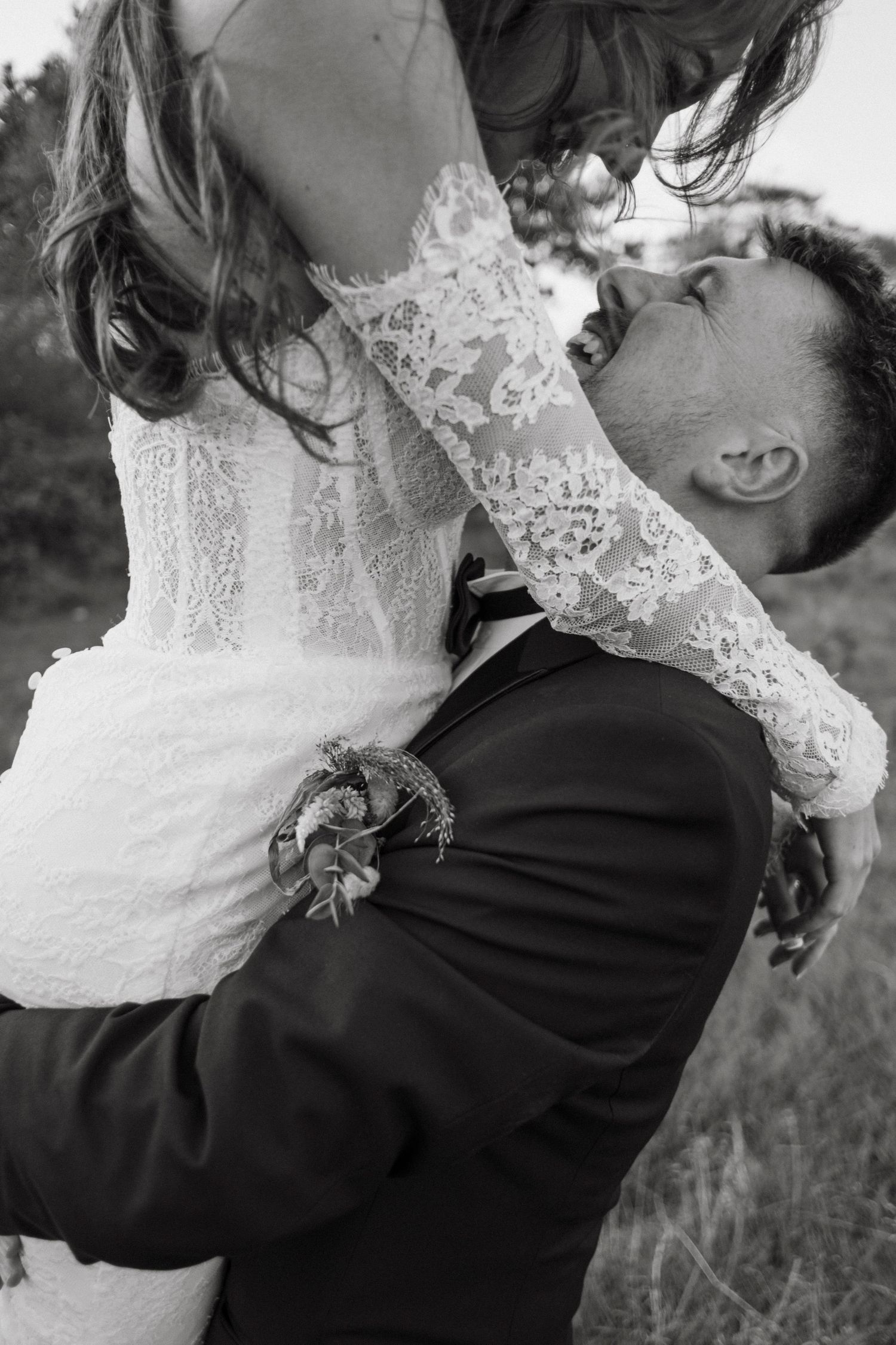 Black and white photo of groom lifting his bride in a lace wedding dress outdoors.
