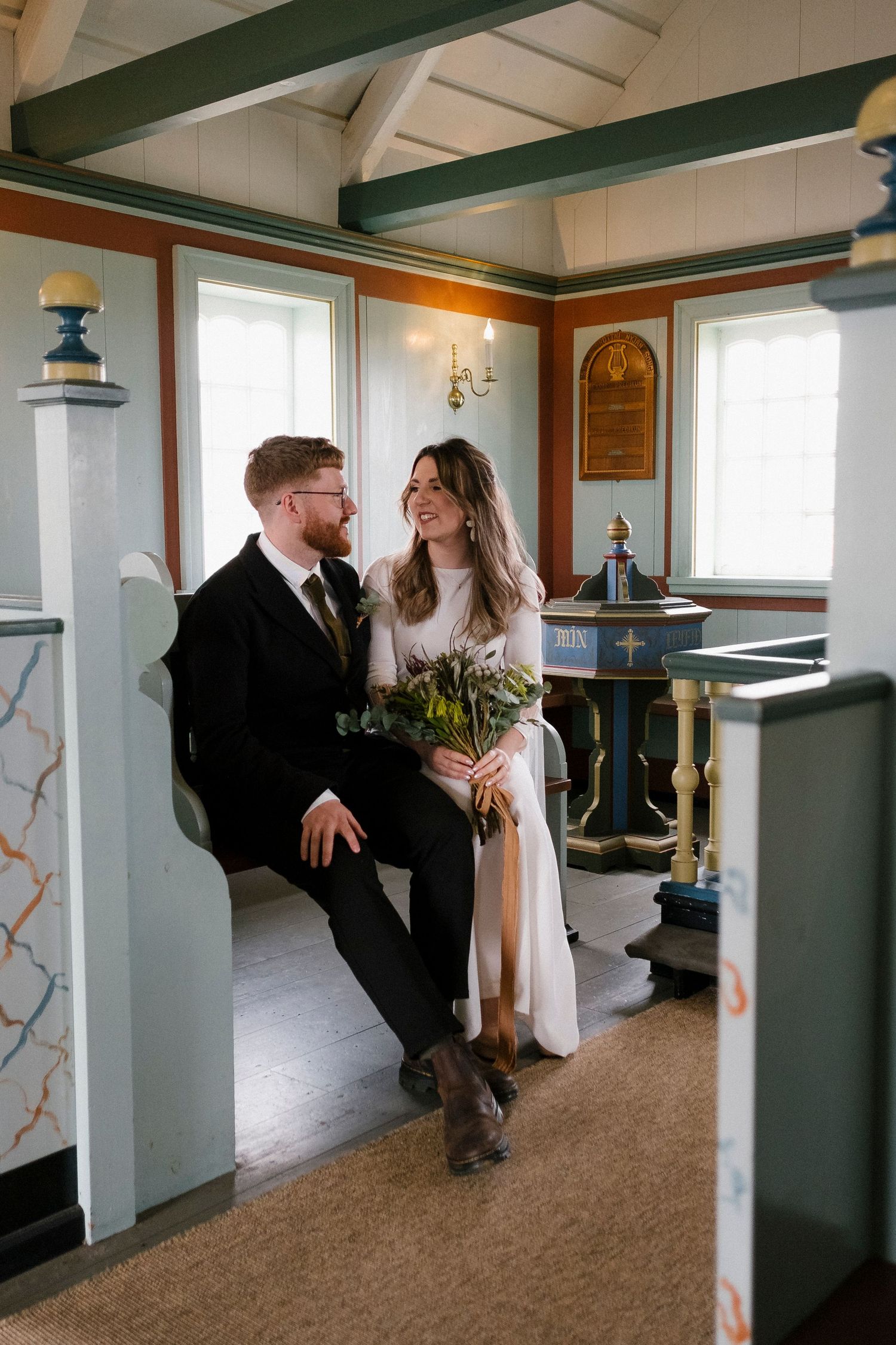 Bride and groom sitting together inside a charming rustic church interior.