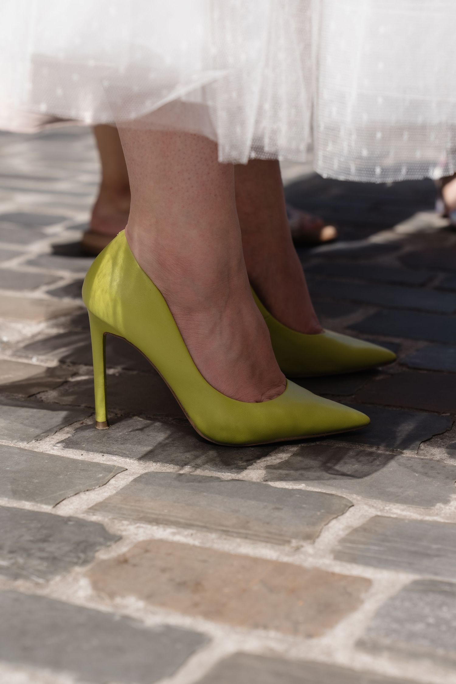 Bride wearing stylish neon yellow-green stiletto heels with a white tulle wedding dress on cobblestone.