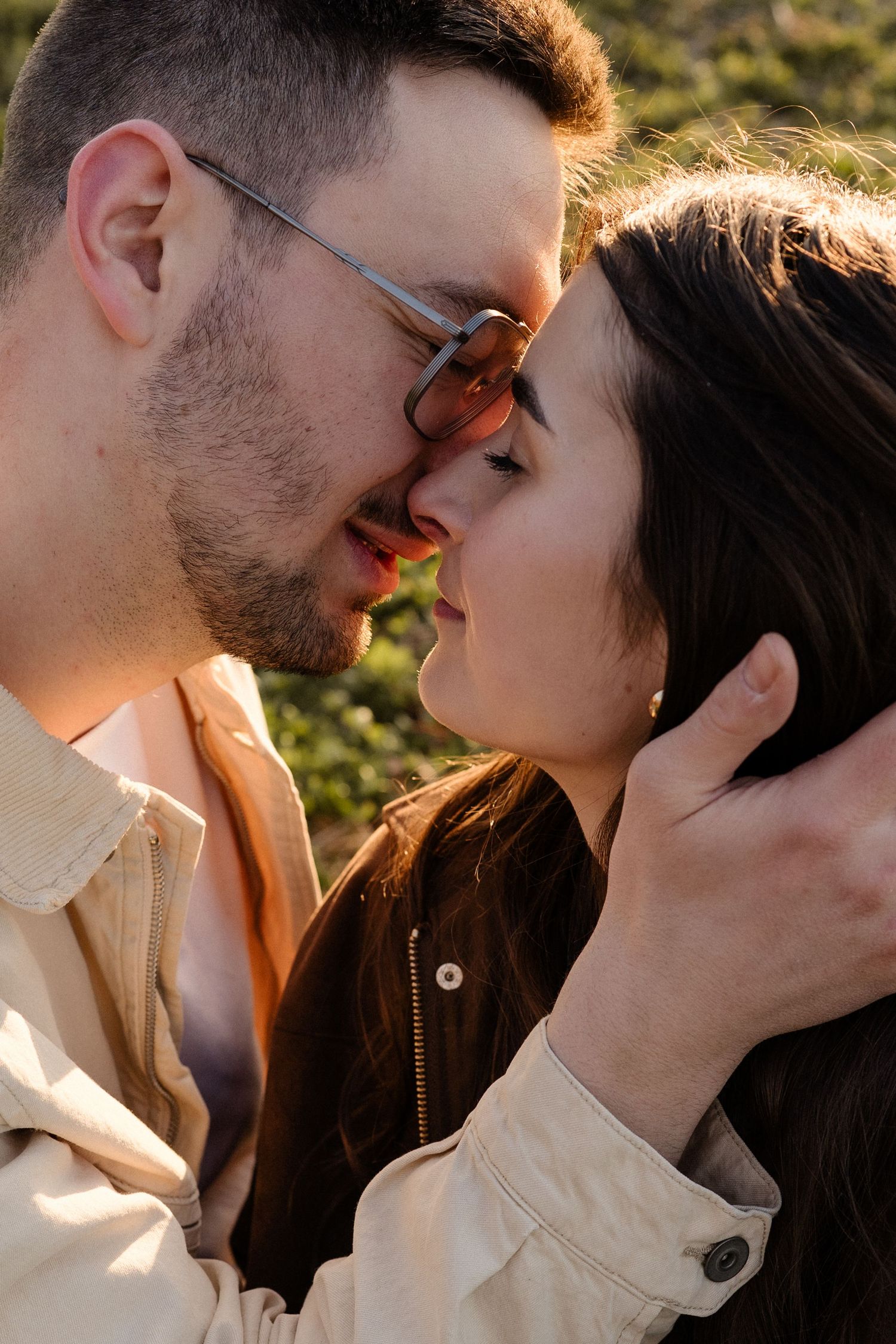Close-up of couple about to kiss, woman wearing sunglasses, bathed in warm natural sunlight.