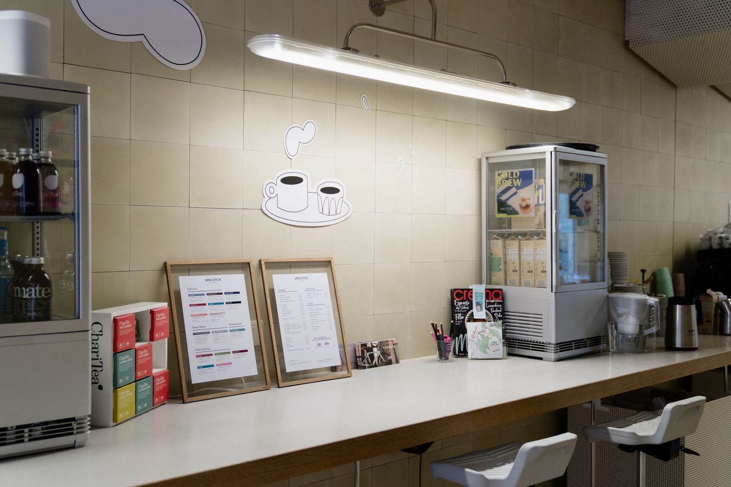 Clean white counter with framed menus, a coffee cup illustration, and appliances on tiled wall.