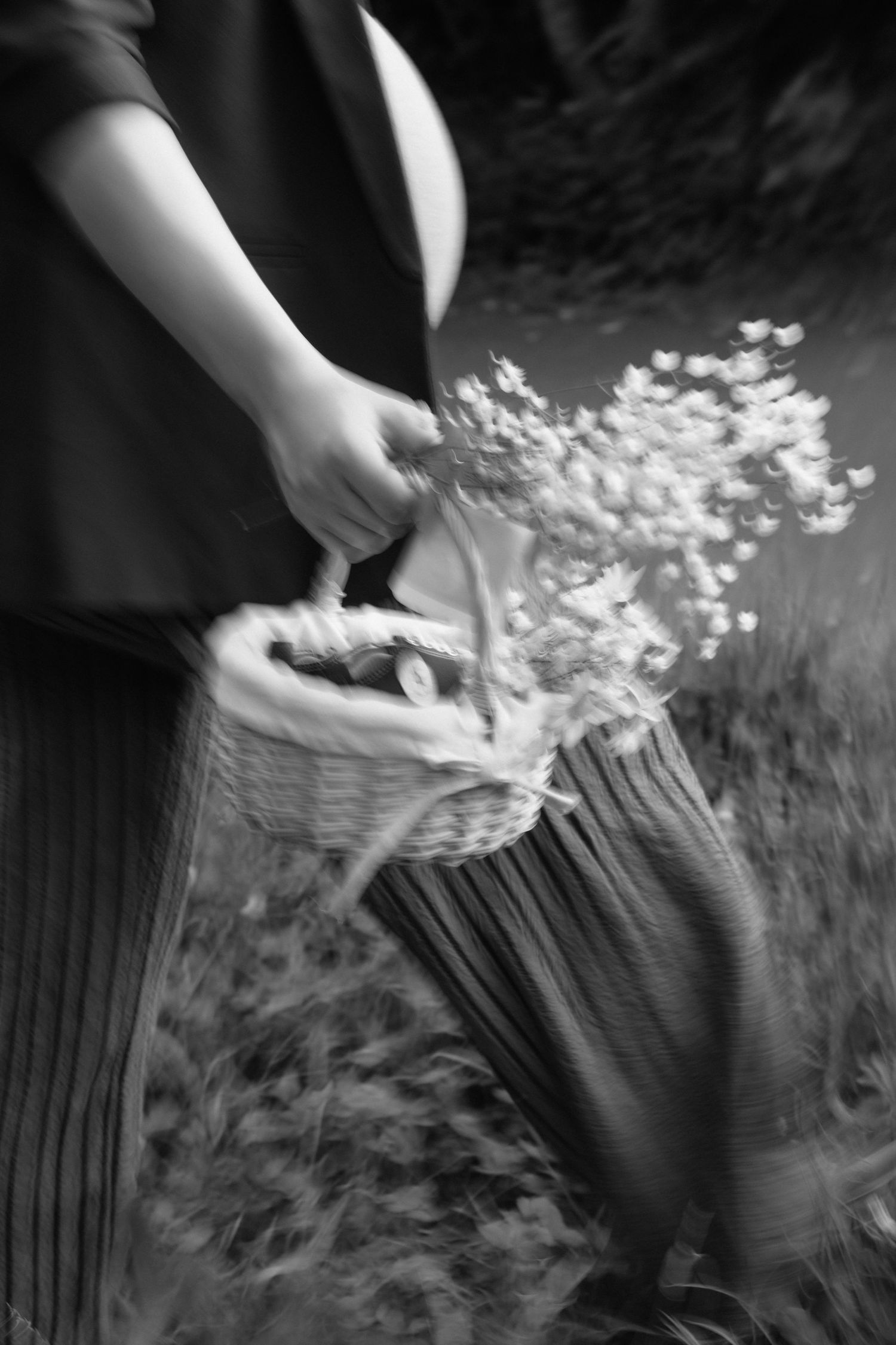 Black and white photo of pregnant woman carrying wicker basket with wildflowers in a garden.