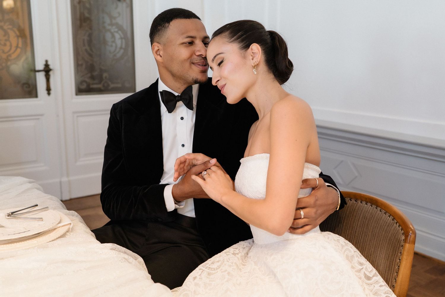 Newlywed couple holding hands and sharing an intimate moment while seated at their wedding reception table.