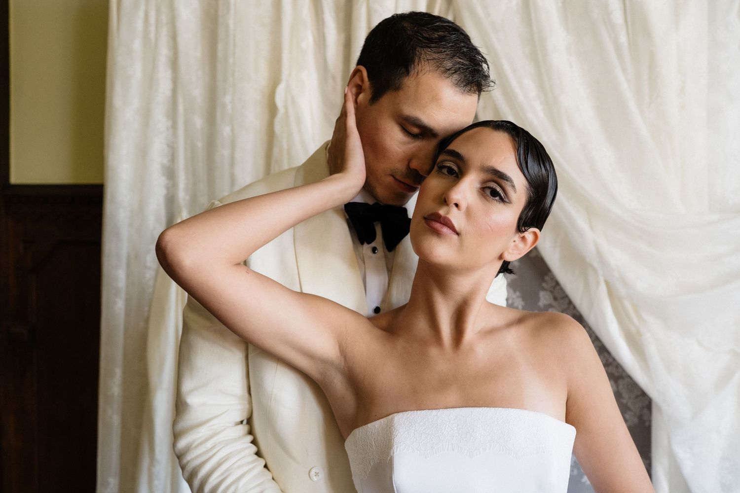 Groom tenderly kisses brides temple as she gazes forward in a romantic portrait.